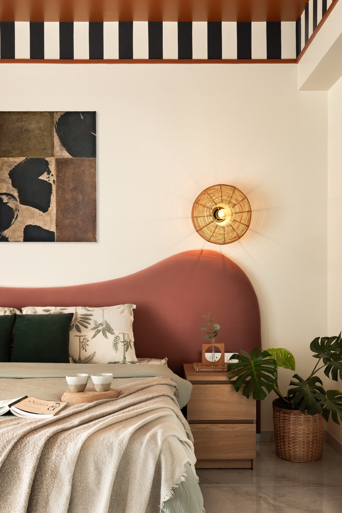 Terracotta curved headboard below a black-and-white striped band and a woven wall light