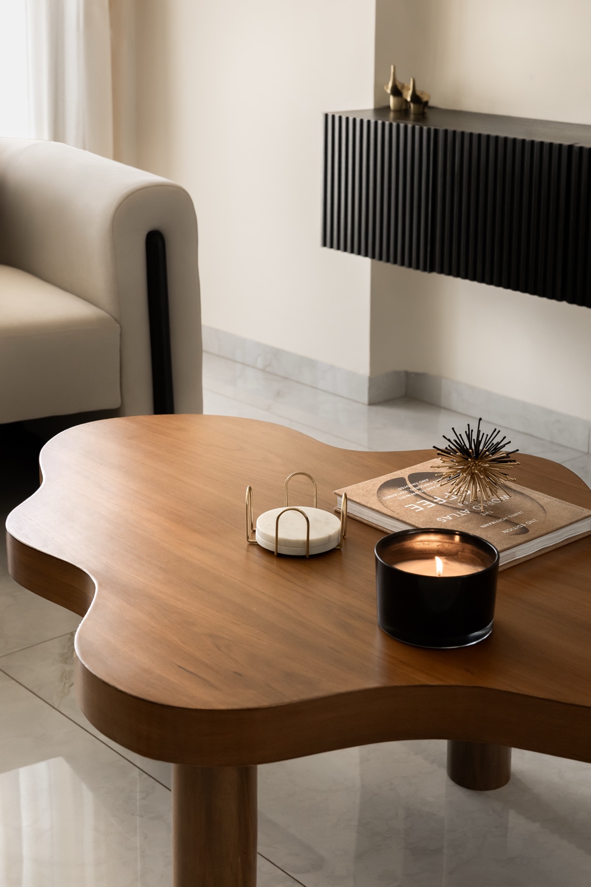 Curved wooden coffee table with a candle and book, against the black fluted console