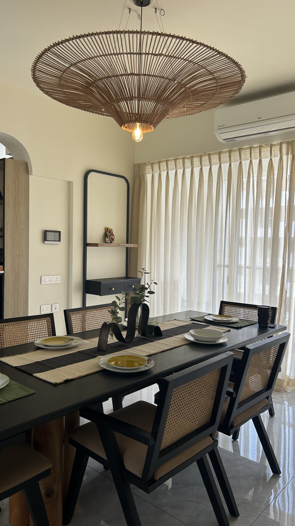 Black dining table and cane chairs under a woven rattan pendant