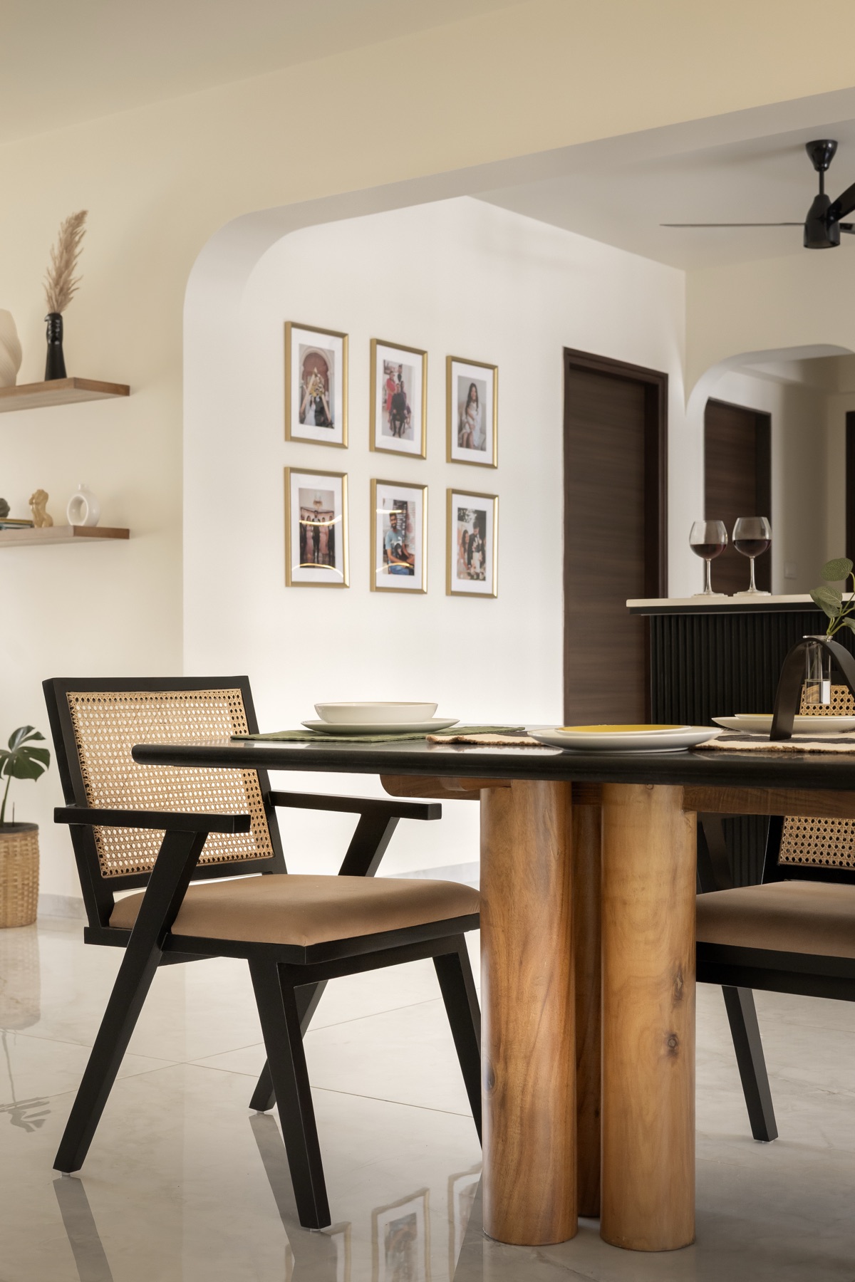 Dining table on a round wooden base with cane-backed chairs and a framed gallery wall behind