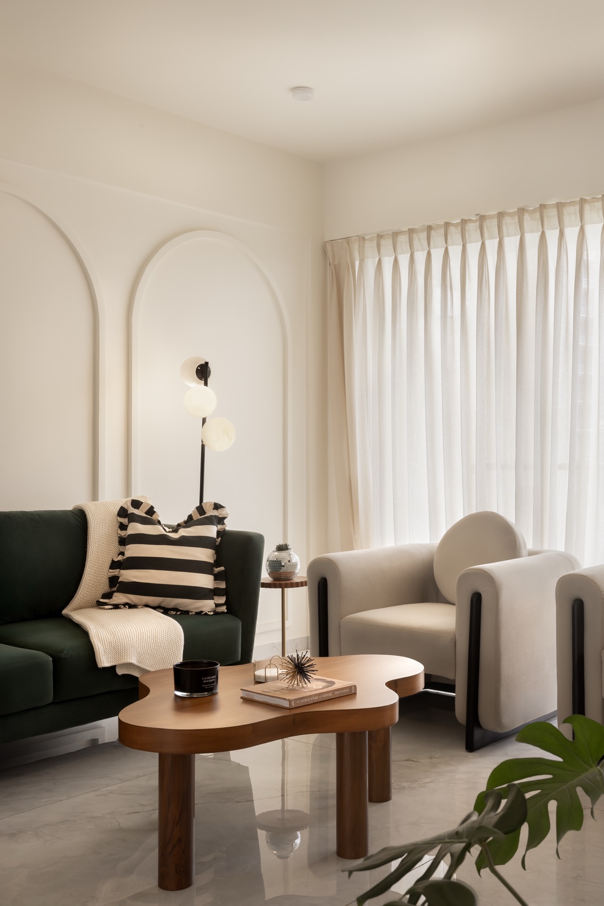 Living room with a deep green sofa, boucle armchair and a curved wooden coffee table beside an arched niche