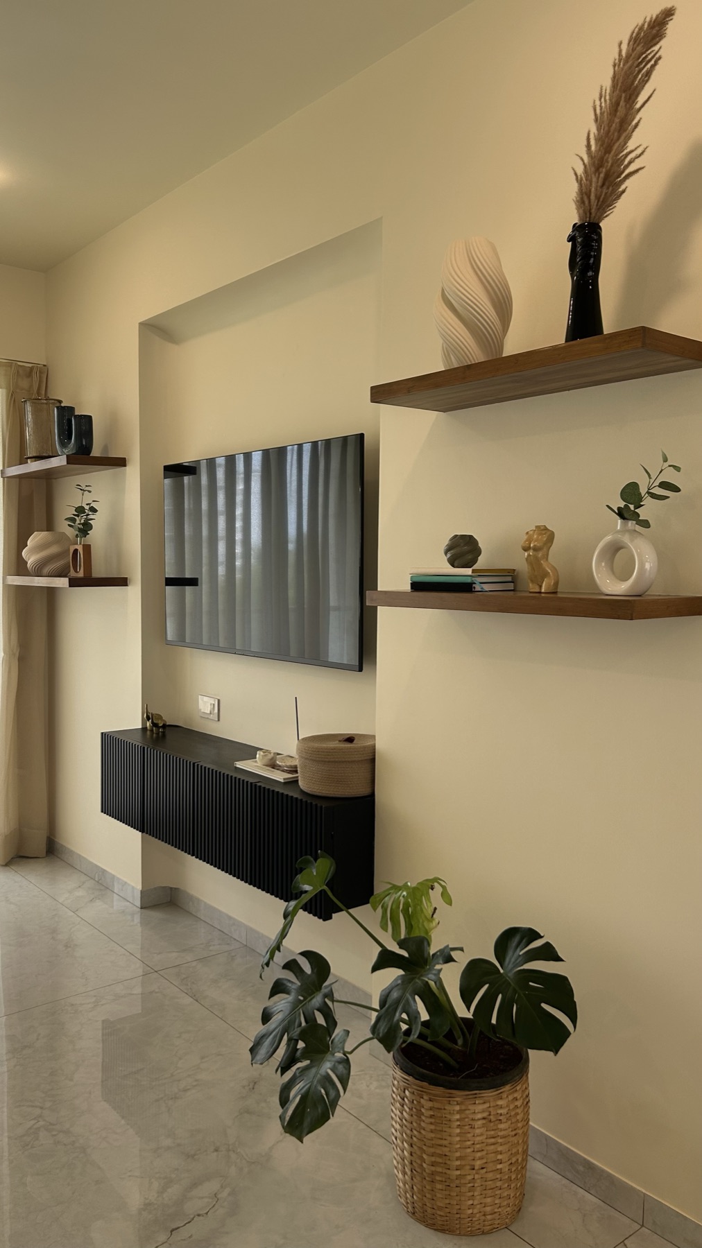 Styled shelves and black fluted console below the television, with dried grasses and a potted plant