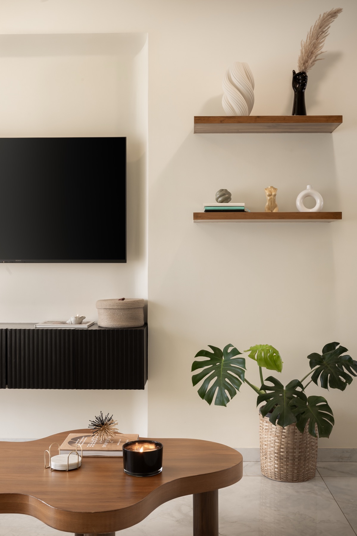 Wall-mounted television above a black fluted console, with floating oak shelves alongside