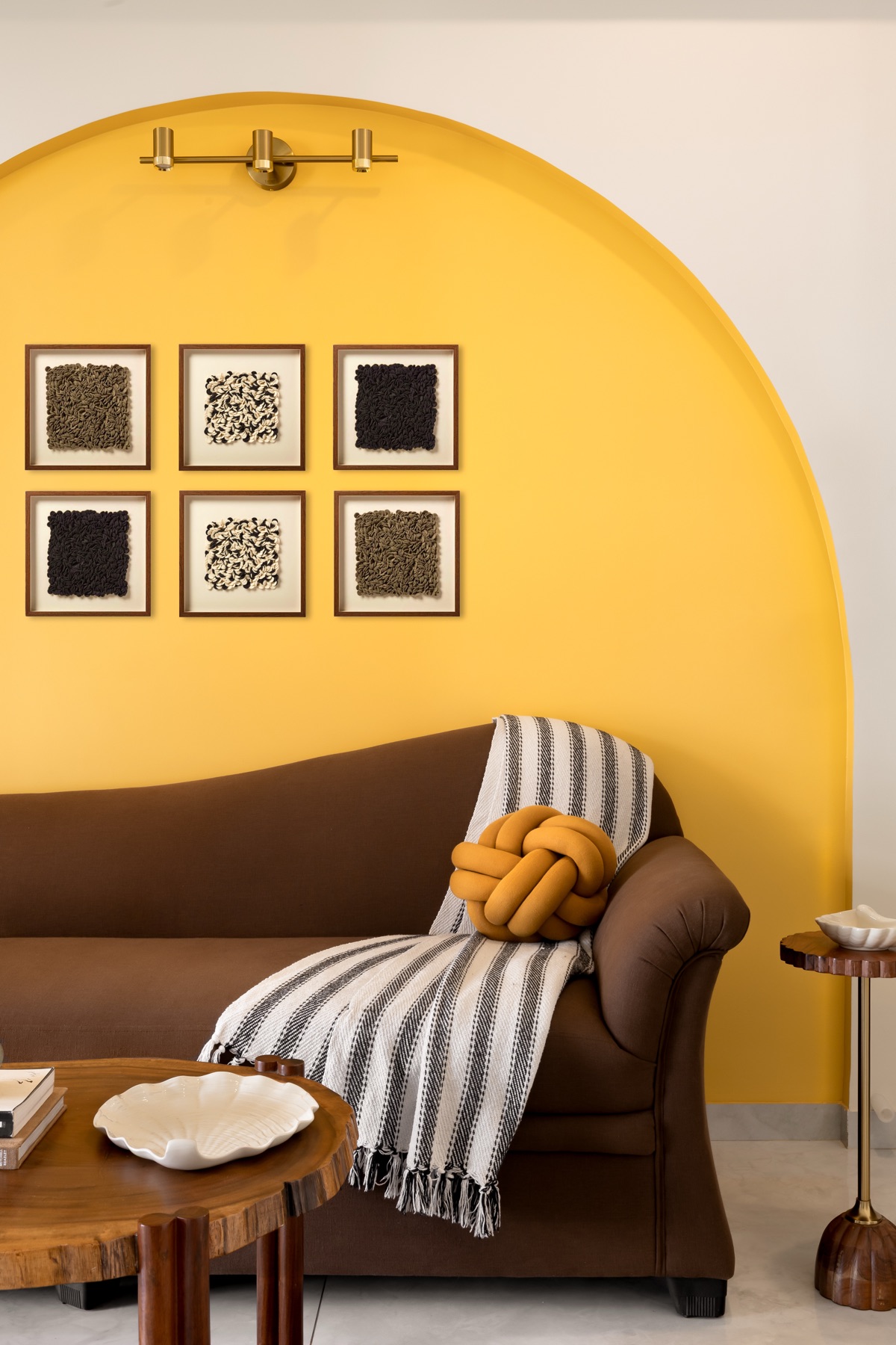 Brown sofa with a knotted cushion set into a painted yellow arch below framed textile art