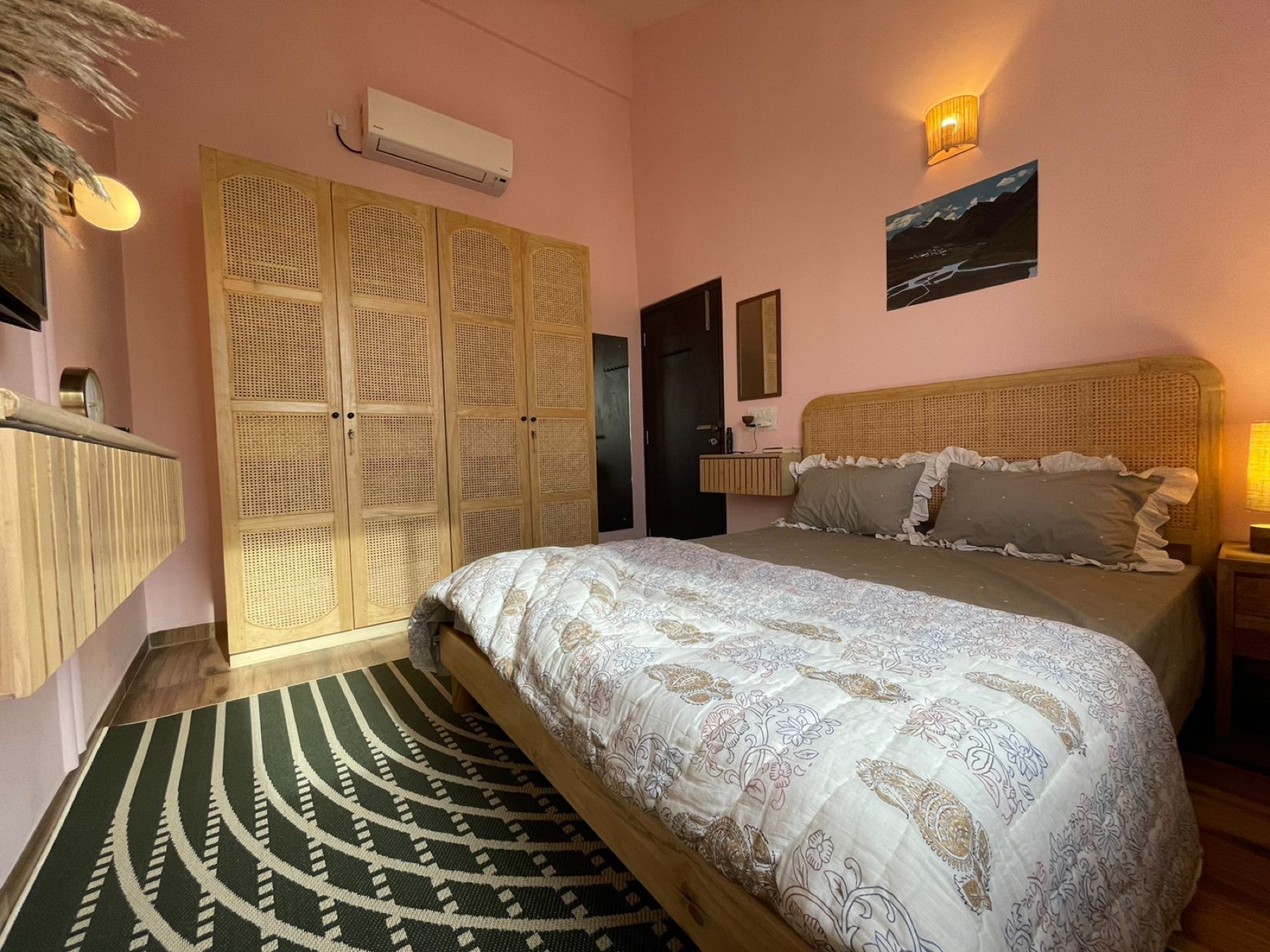 Bed beside cane-fronted wardrobes, with a graphic green and cream rug underfoot