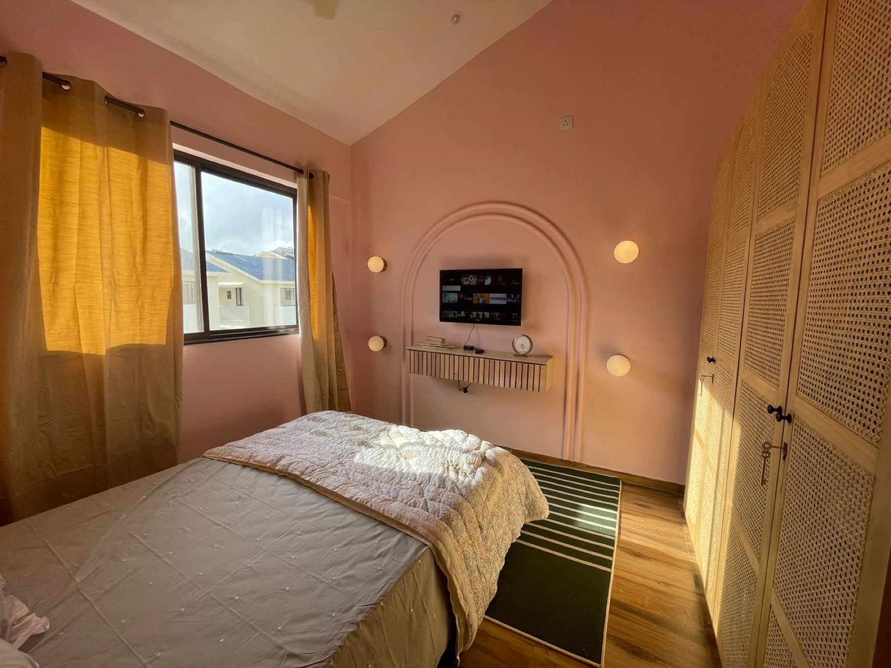 Bedroom in blush pink with an arched alcove for the television and a cane wardrobe