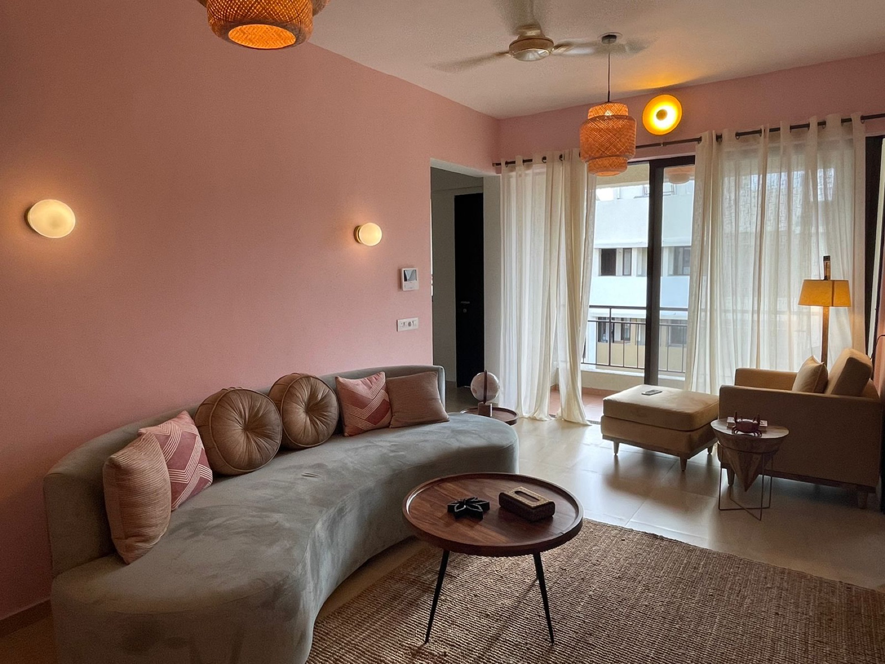 Living room in blush pink with a long curved sofa, round wooden table and balcony beyond