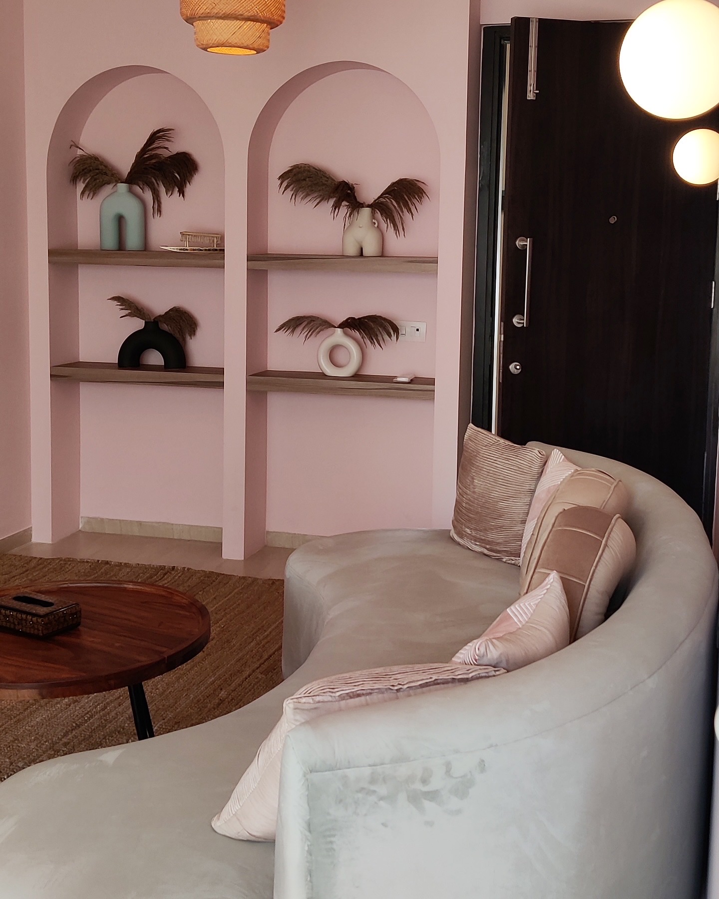 Arched display niches in blush pink beside the curved sofa