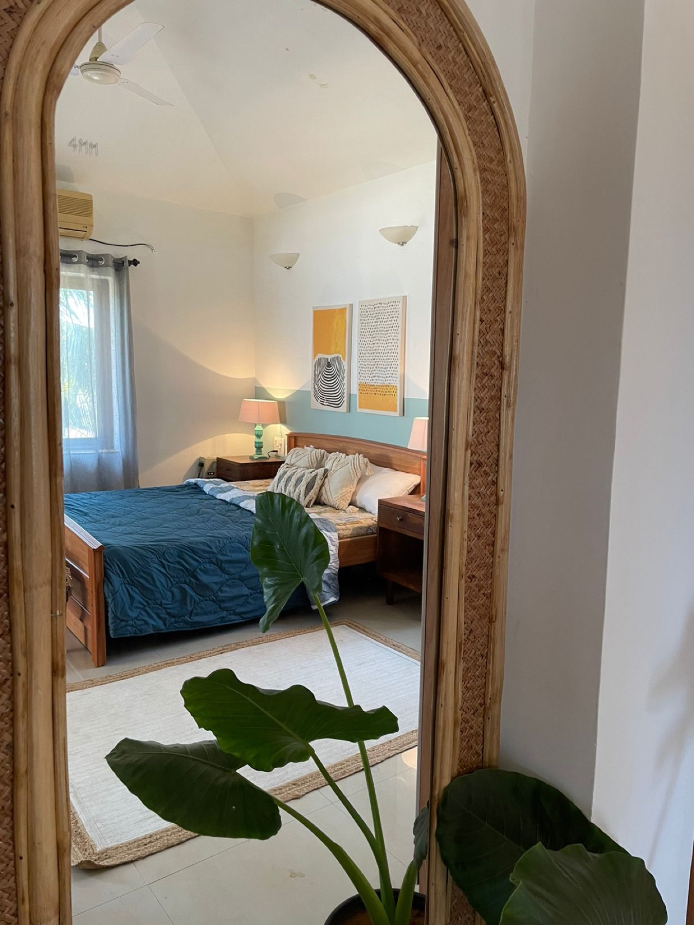Arched timber mirror reflecting the teal bedroom and its framed prints