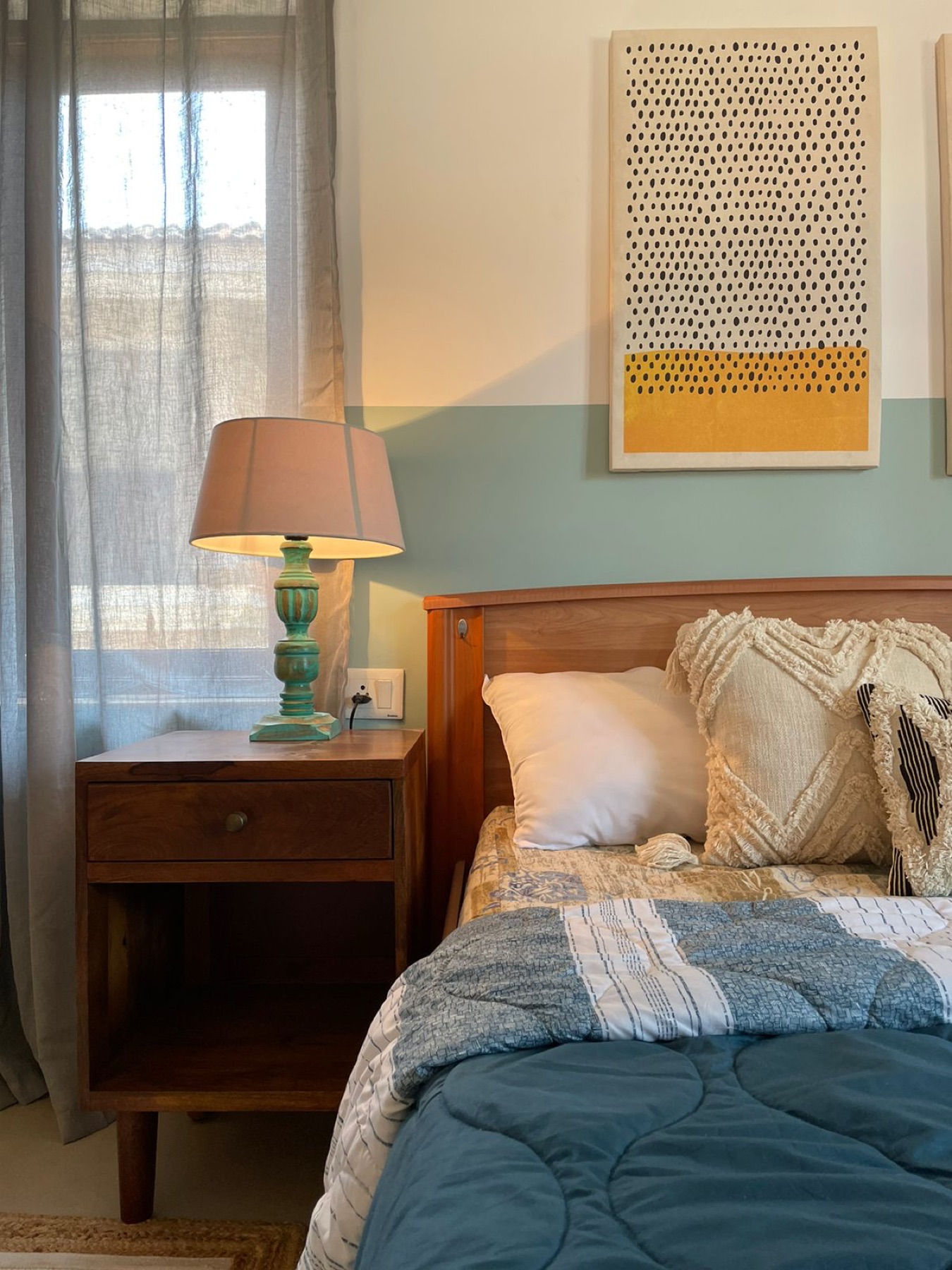 Teak bed dressed in teal against a sage wall band, with a green glass lamp alongside