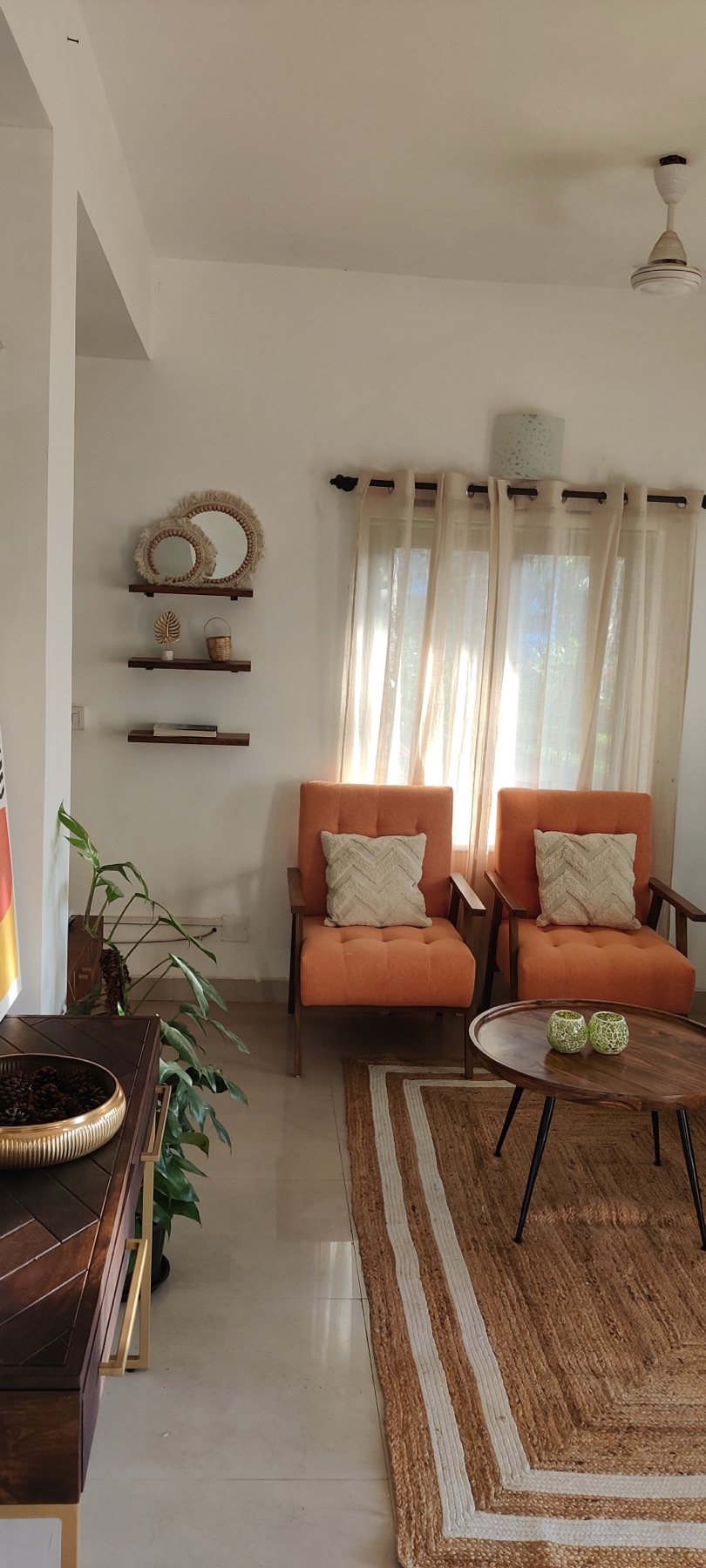 Floating shelves and greenery beside the orange armchairs and round wooden table