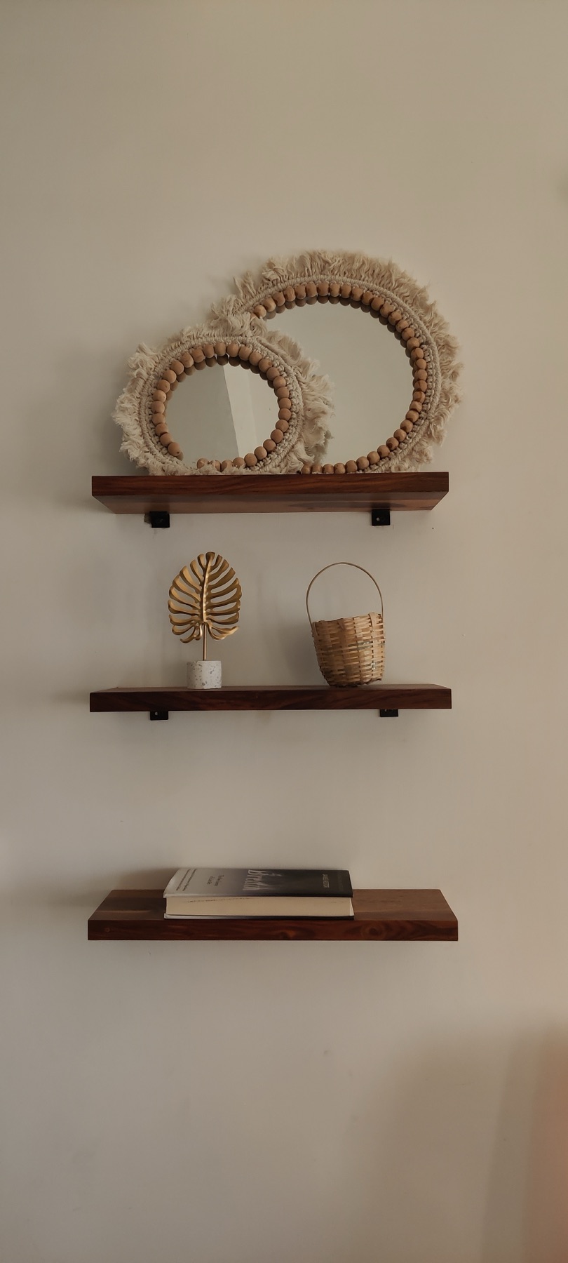 Rattan-fringed mirrors above slim walnut shelves holding woven objects