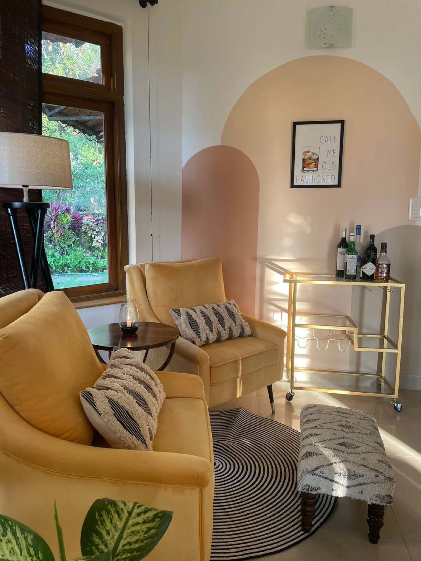 Mustard armchairs beside an arched alcove with a brass bar cart and garden window