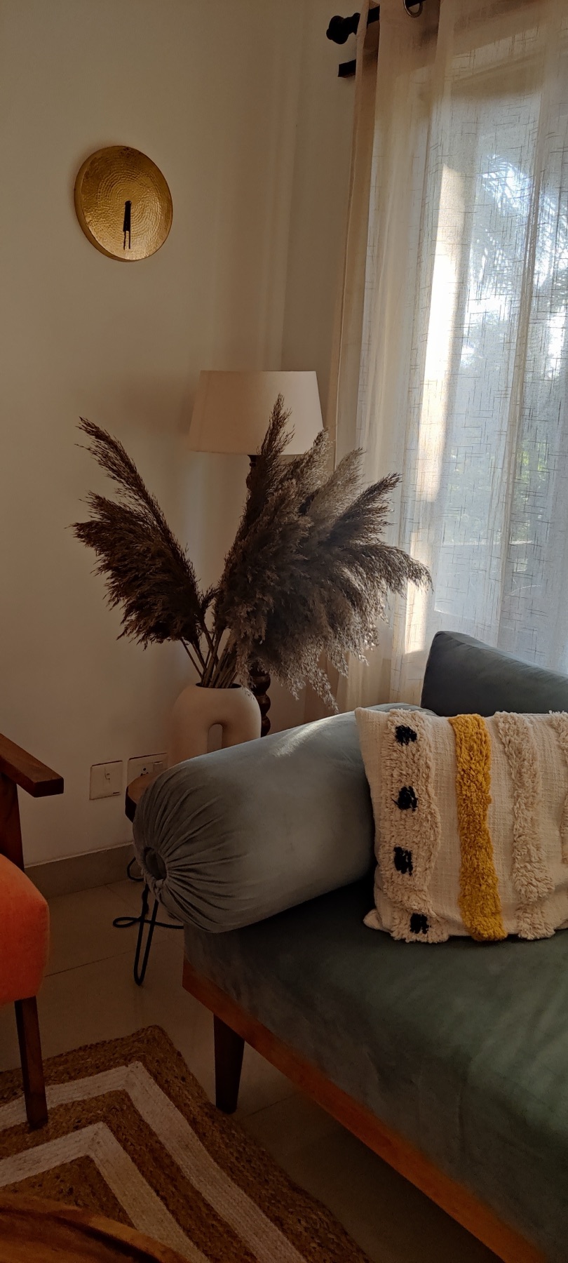Teak-framed sofa in sage green with a tufted mustard cushion, pampas grass behind