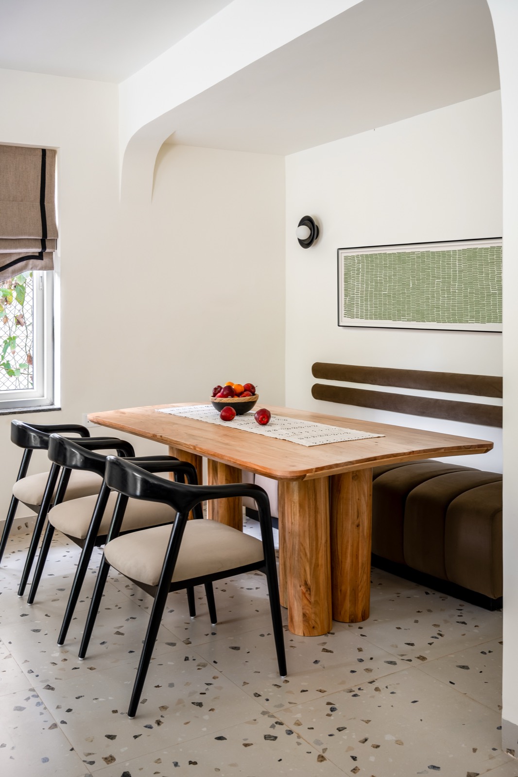 Dining table in solid wood with black chairs, a built-in bench and terrazzo flooring