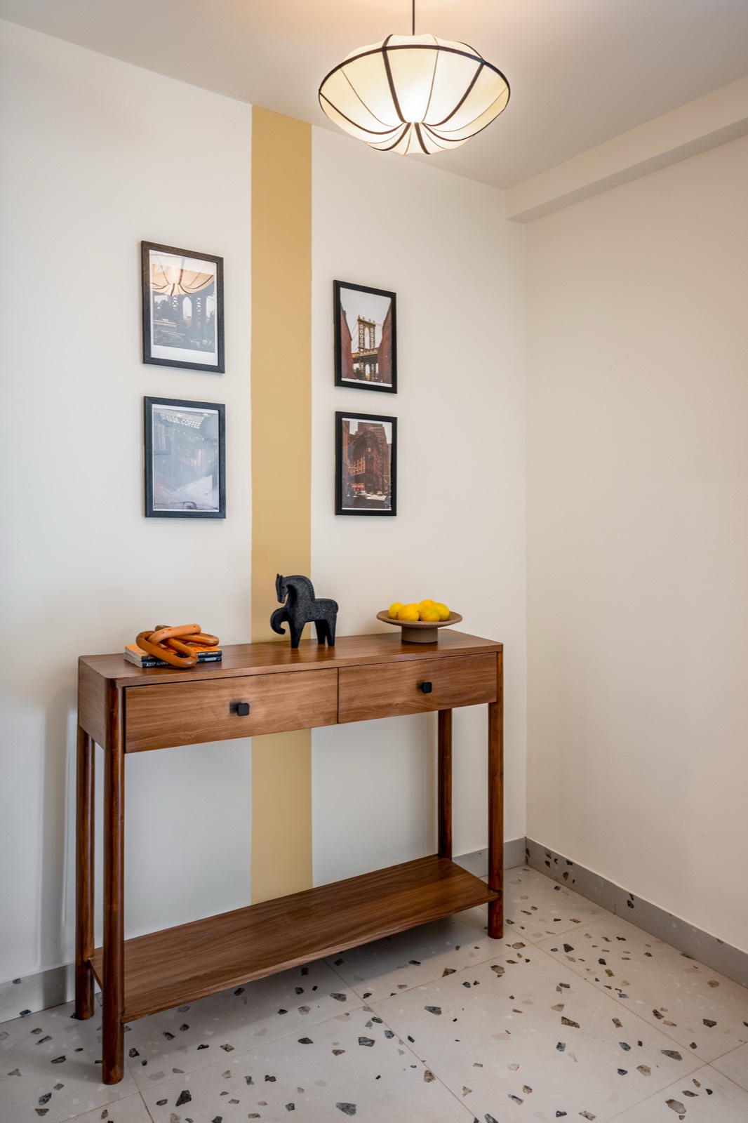 Entry console in teak below a pleated pendant, with a single mustard band running floor to ceiling