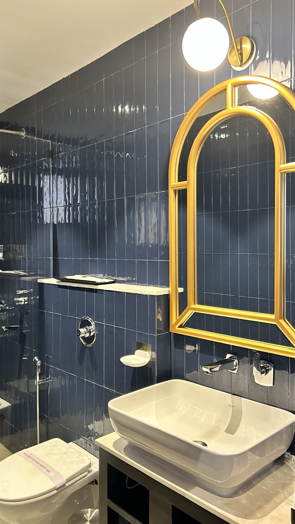 Navy tiled bathroom with a gold arched mirror above the stone basin
