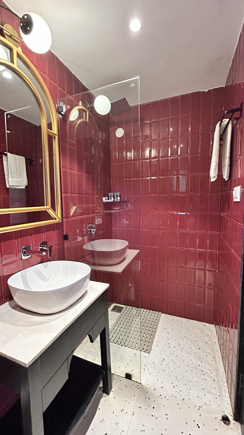 Oxblood tiled bathroom with a gold arched mirror and terrazzo floor