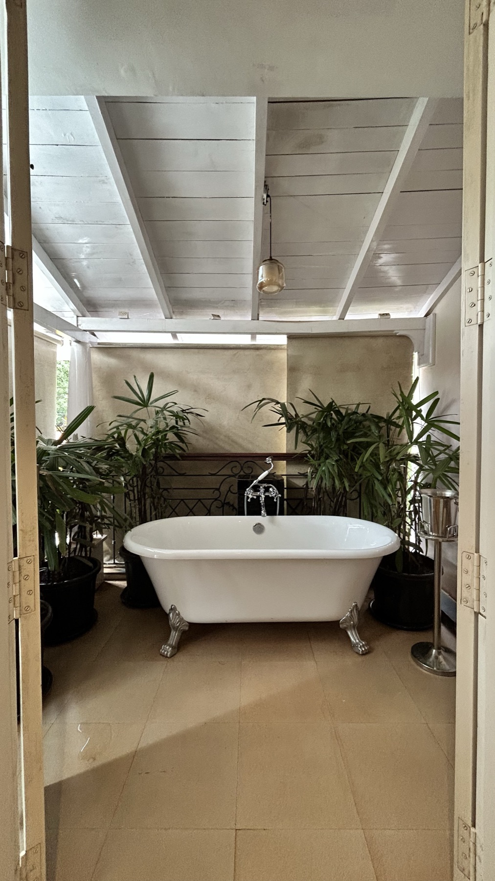 Freestanding clawfoot bath set between planting under a slatted ceiling