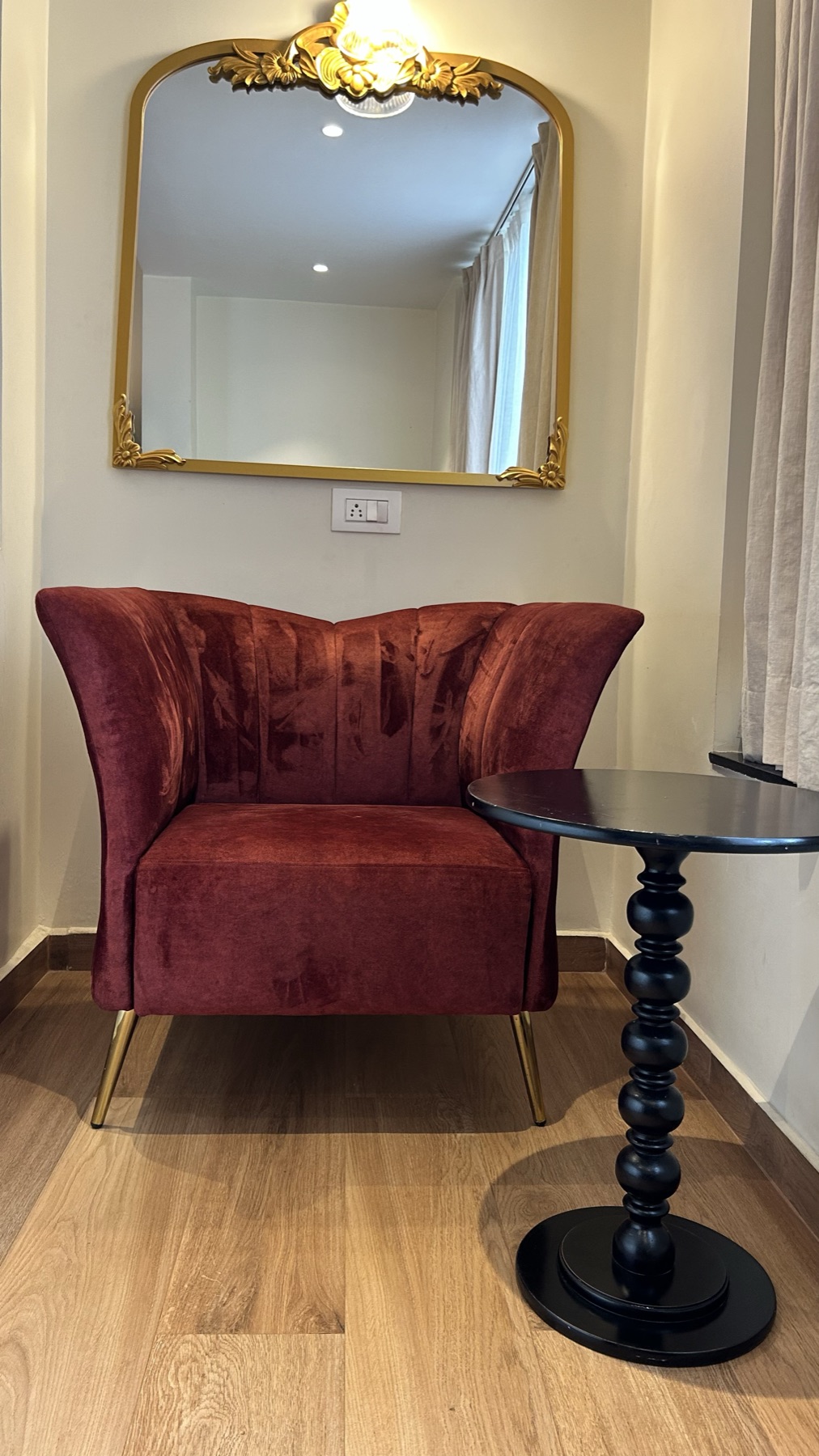 Burgundy velvet chair and black bobbin table below a gilt mirror