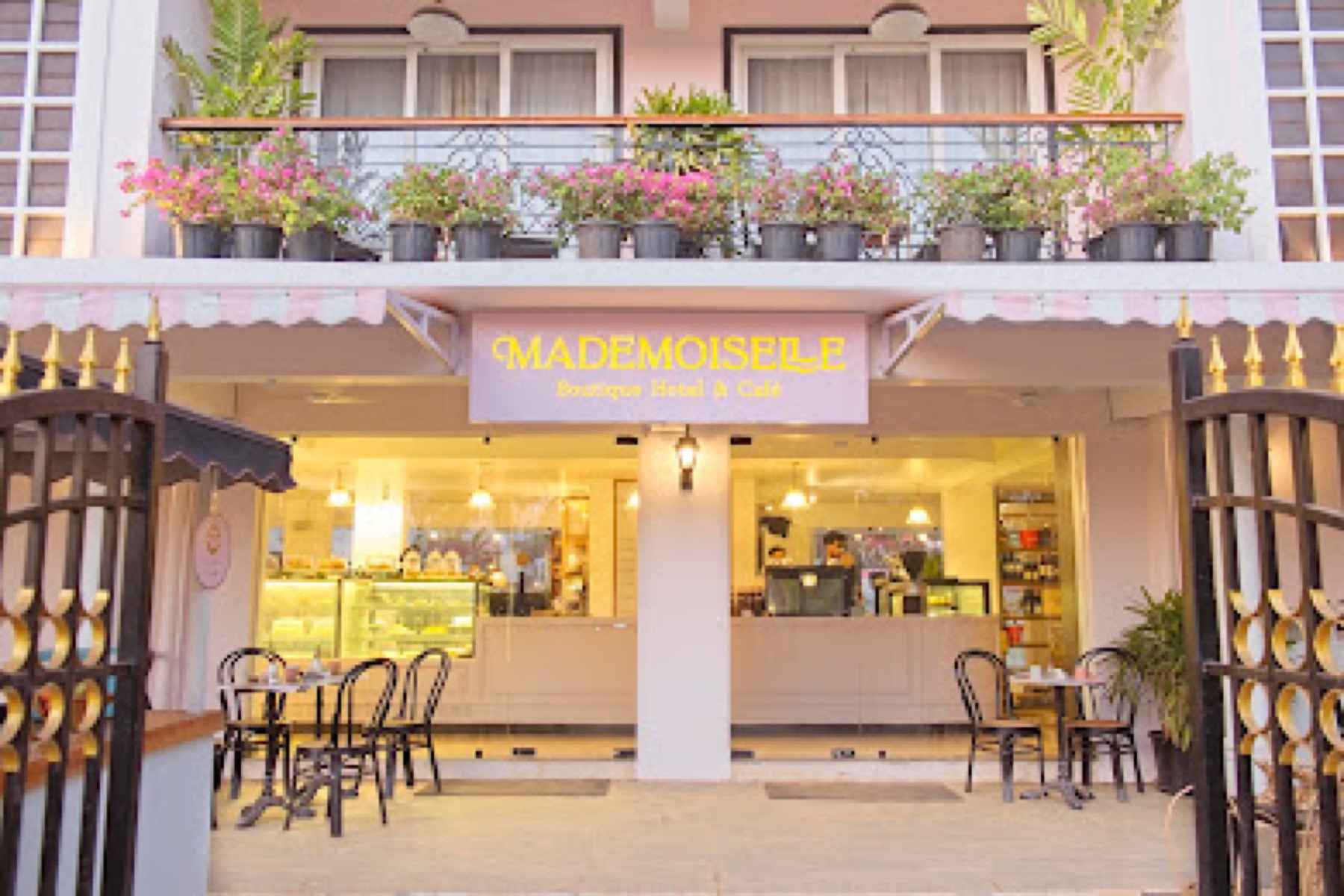 Street frontage with the café behind glass, bougainvillea spilling from the balcony above