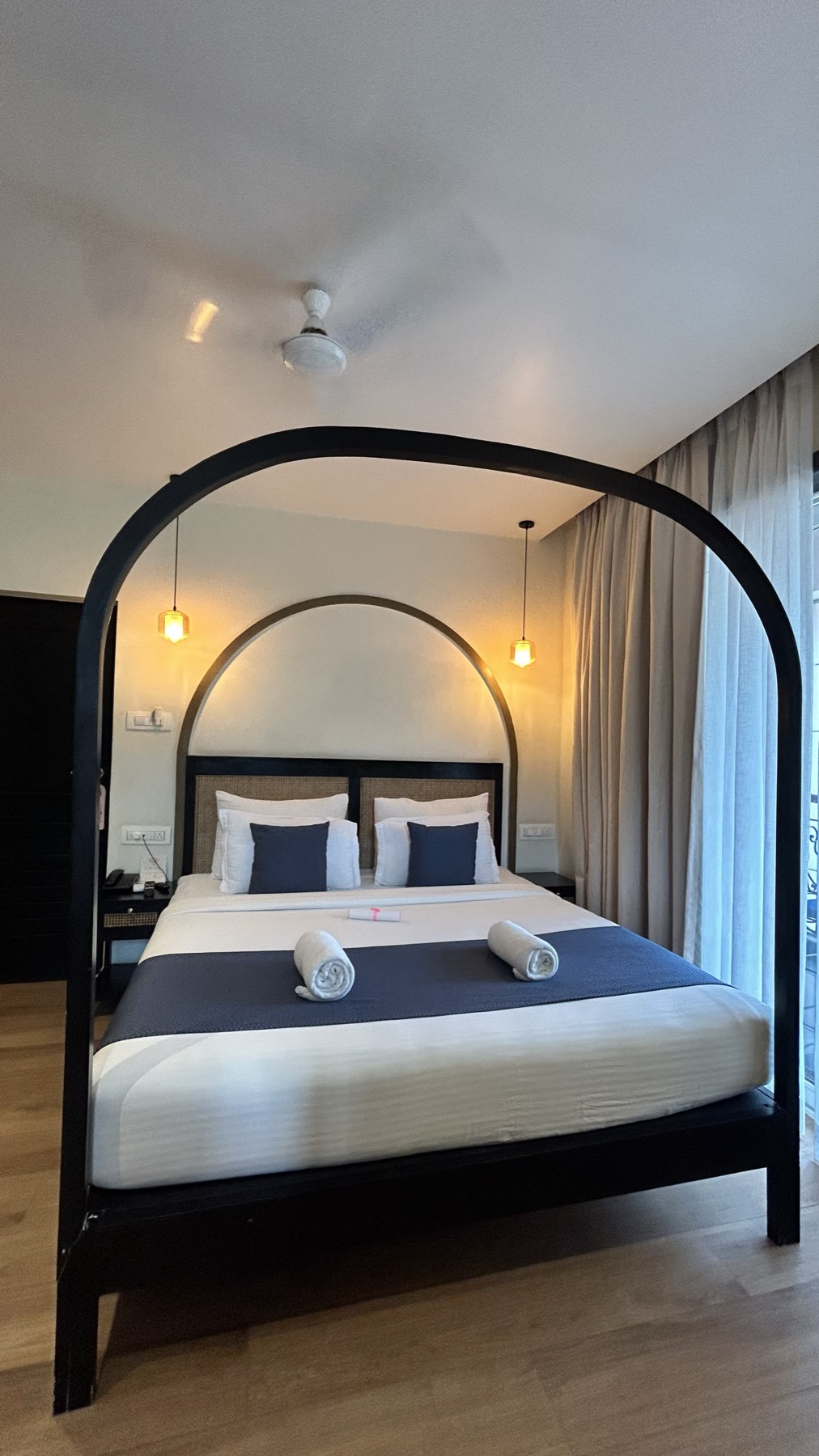 Black arched four-poster frame over navy bedding, lit by a single pendant
