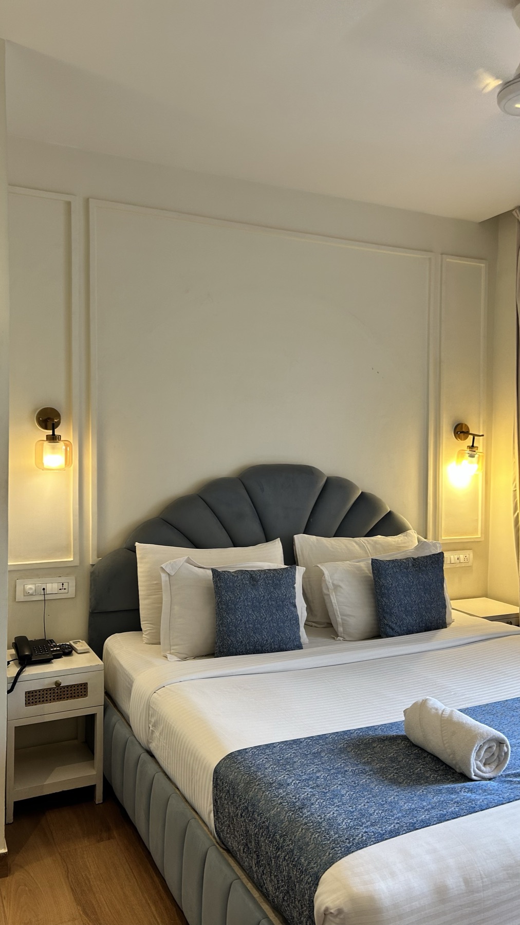Scalloped headboard and navy throw in a panelled room with brass sconces