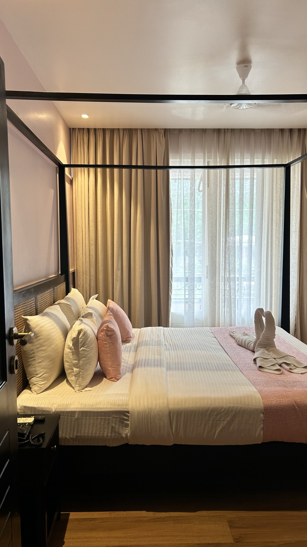 Black four-poster bed dressed in blush and white against panelled walls