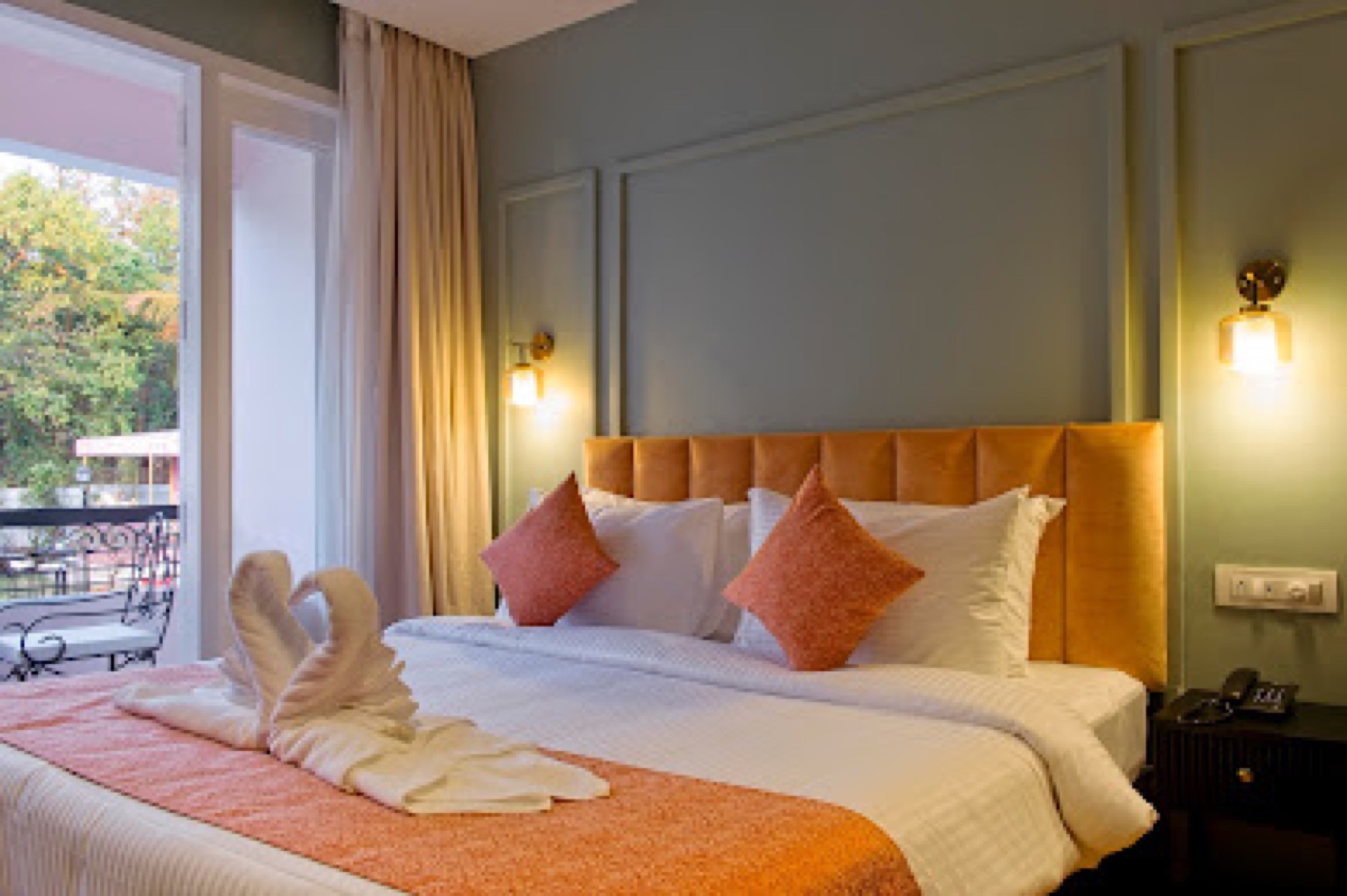 Guest room with a rust upholstered headboard, coral cushions and towel swans