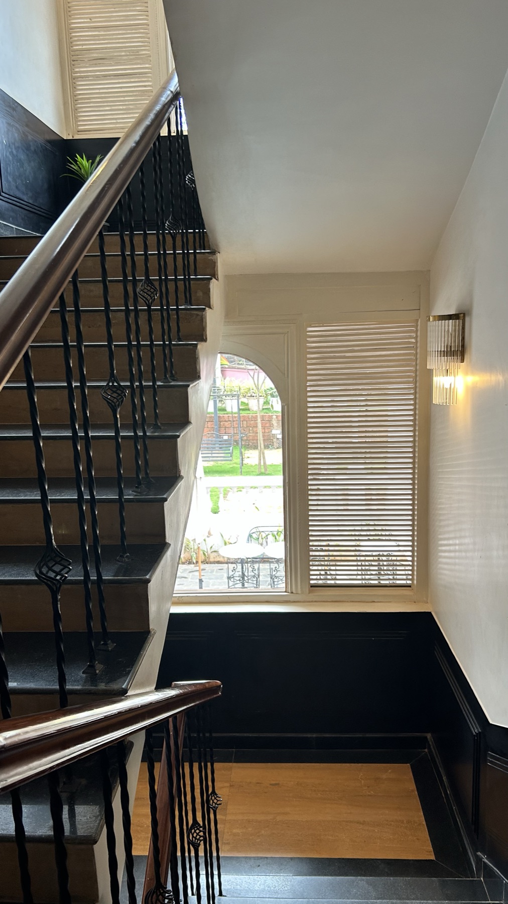 Black steel stair rising past an arched window in the white stairwell
