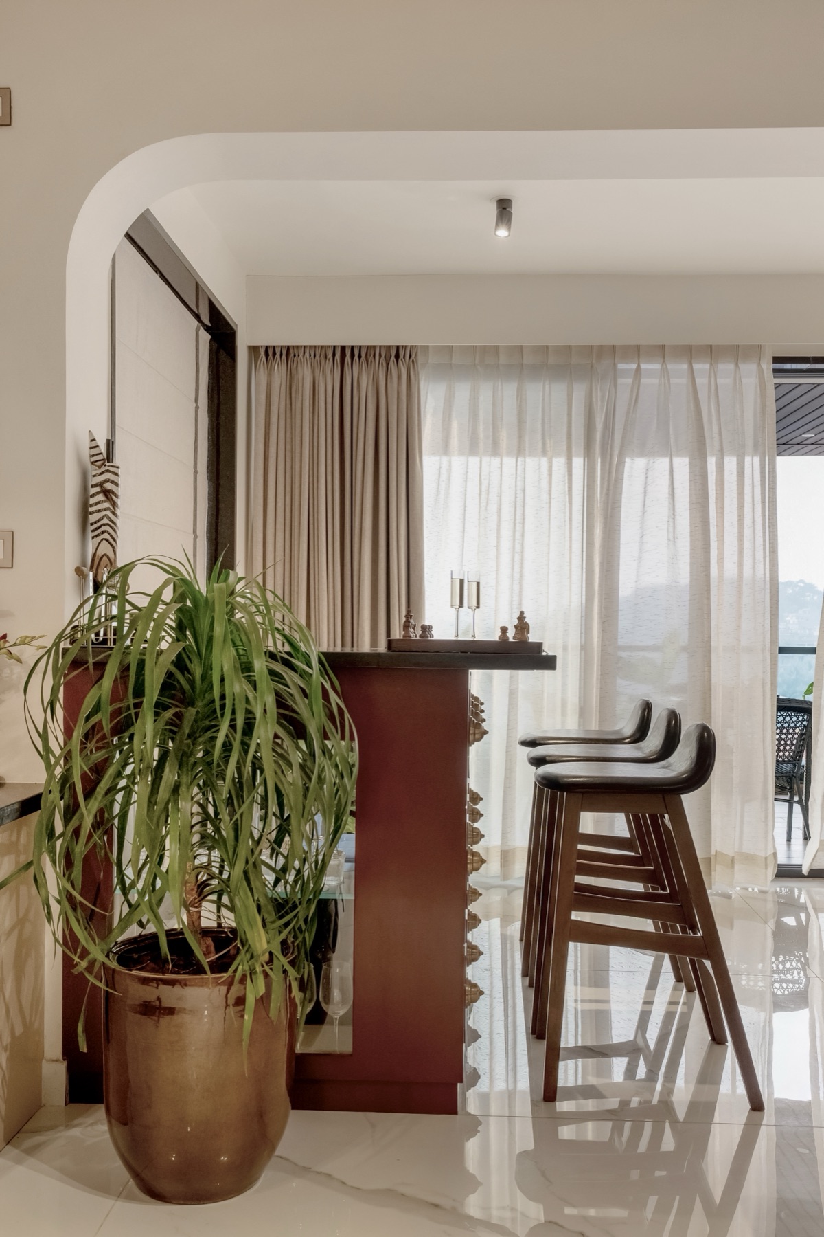 Breakfast counter in oxblood timber with cane-seated stools against the daylit balcony