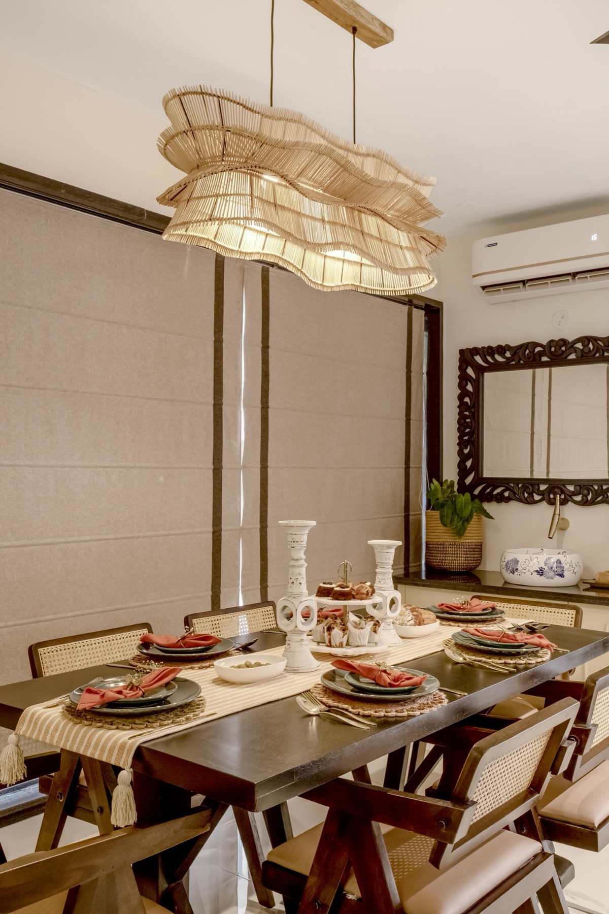 Dining table and cane chairs beneath the woven pendants, seen across the marble floor
