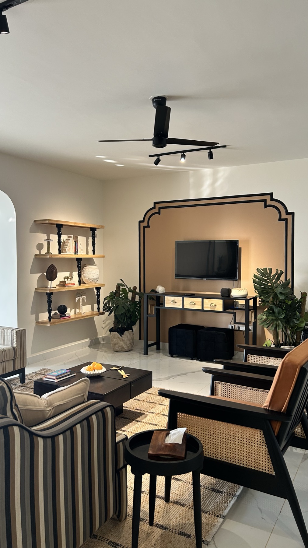 Living room television set into an arched black frame, with open shelving and a striped bench