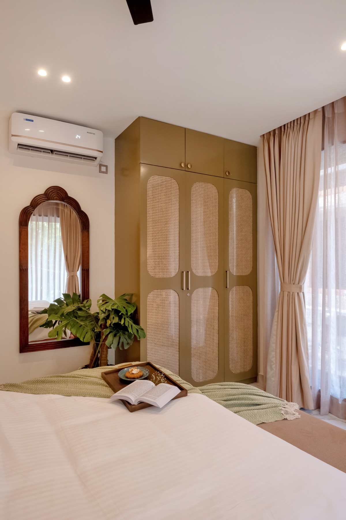 Olive wardrobes beside a carved arched mirror and a potted palm
