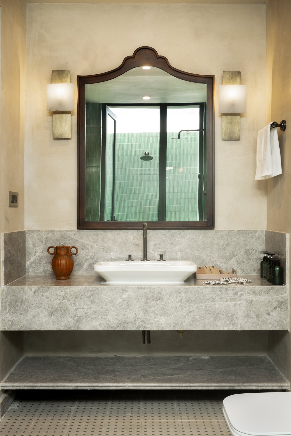 Grey marble vanity below an arched mirror set between two sconces