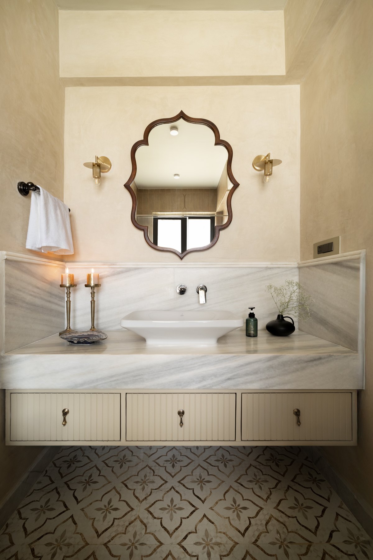 Scalloped mirror above a marble vanity and a patterned tile floor