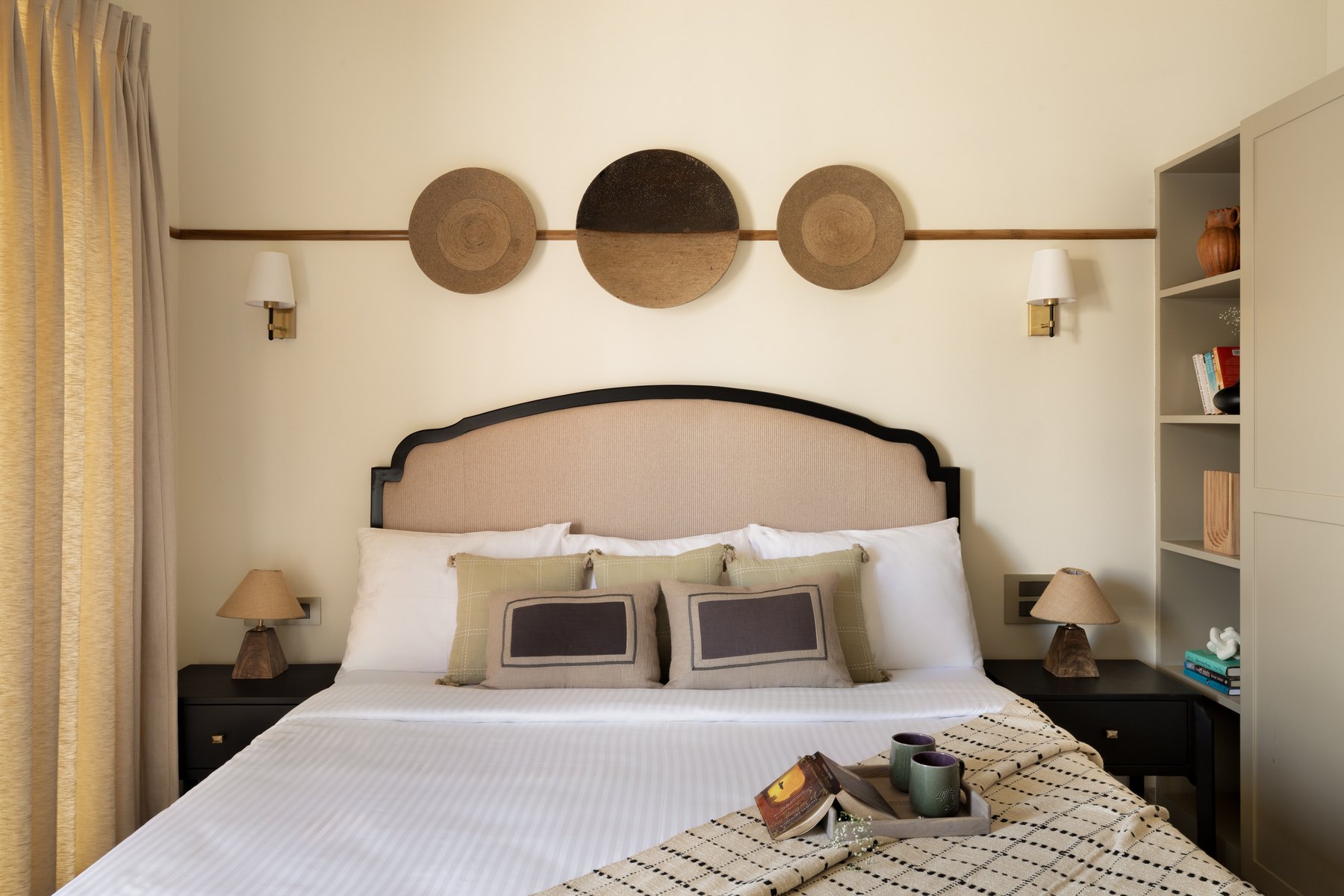 Bed below three woven discs, flanked by black bedside tables and shaded lamps