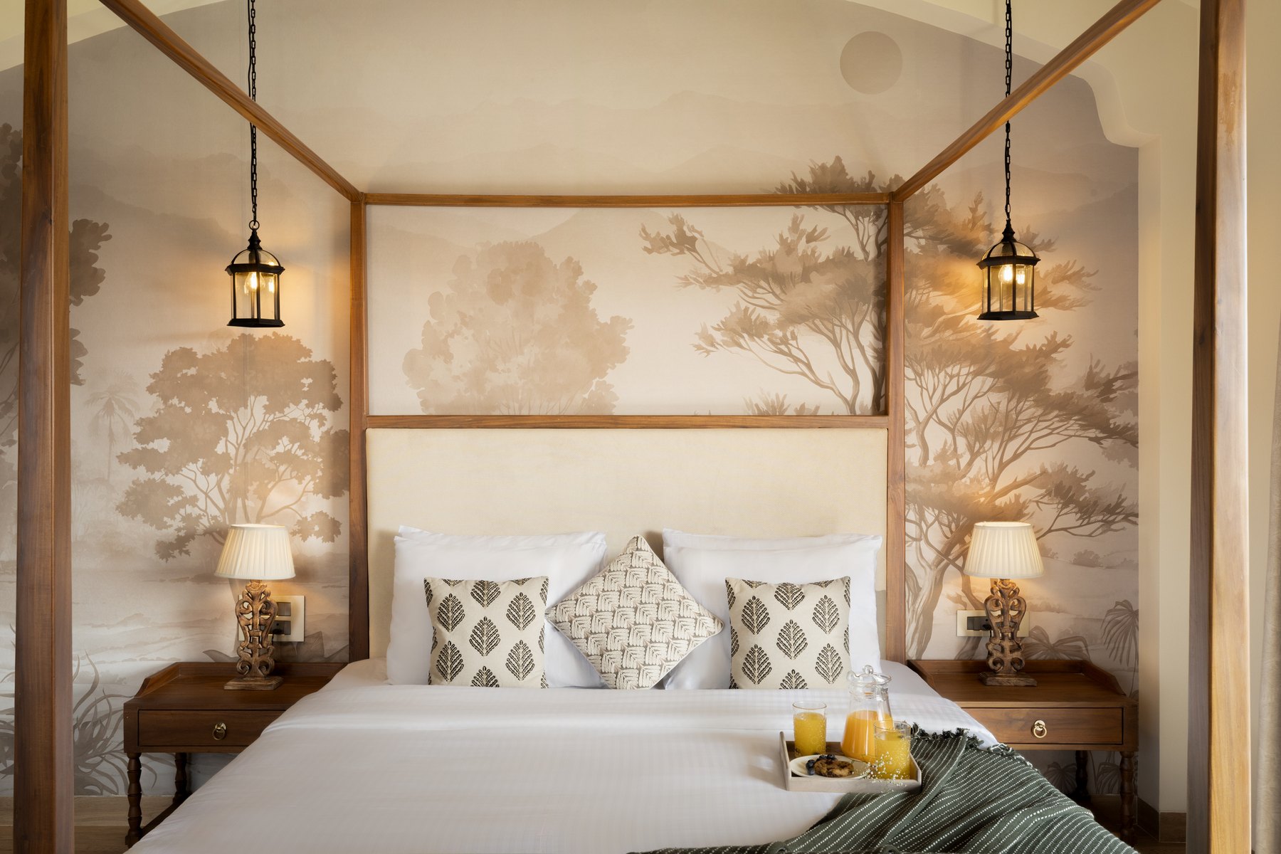 Four-poster bed against a painted tree mural, lanterns hanging to either side