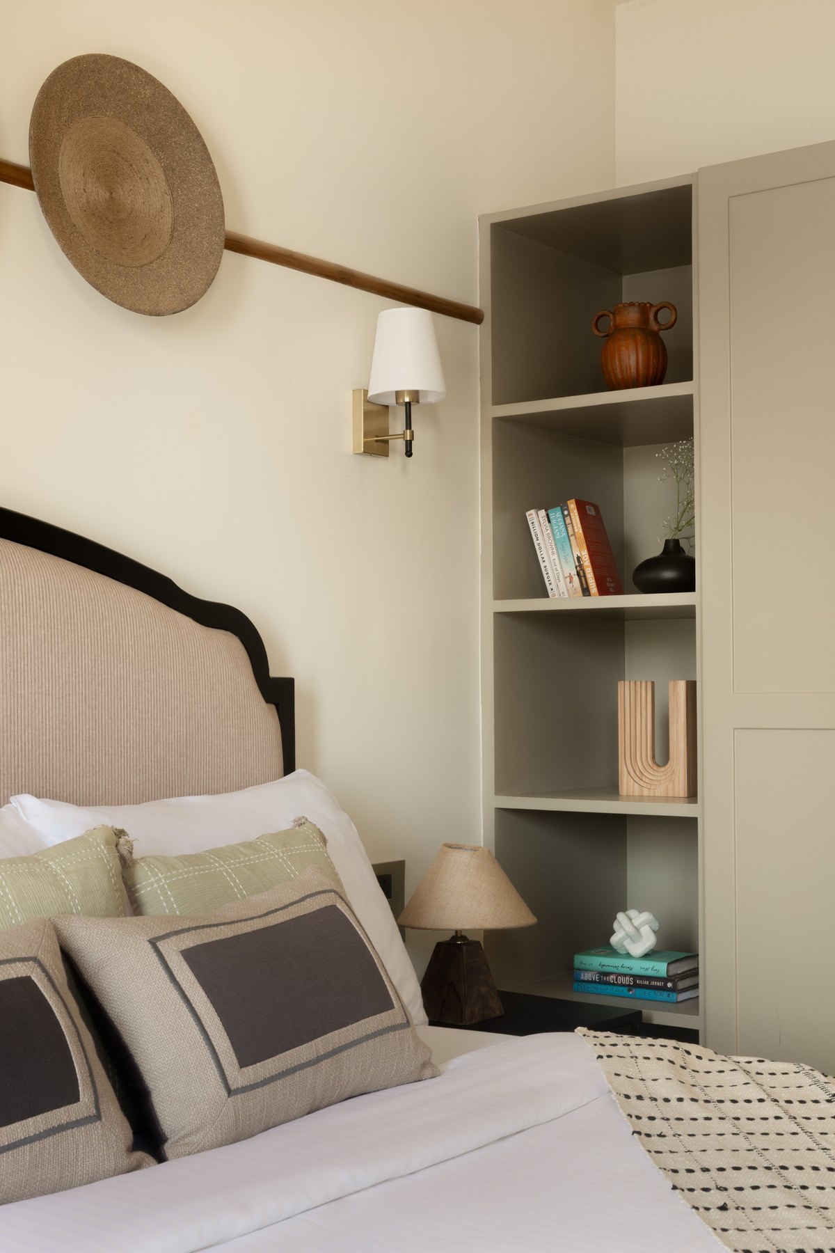 Bed corner with a woven hat on the wall and a niche of books alongside