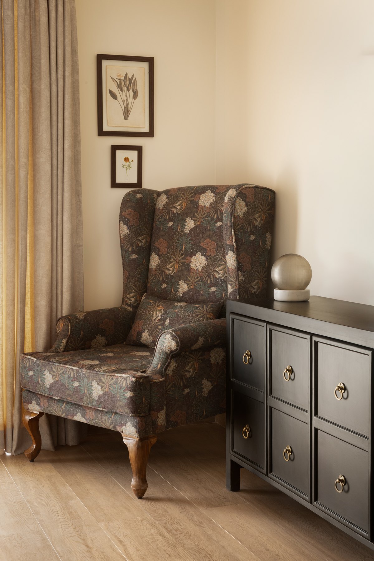 Floral wing chair beside a brass-handled chest of drawers