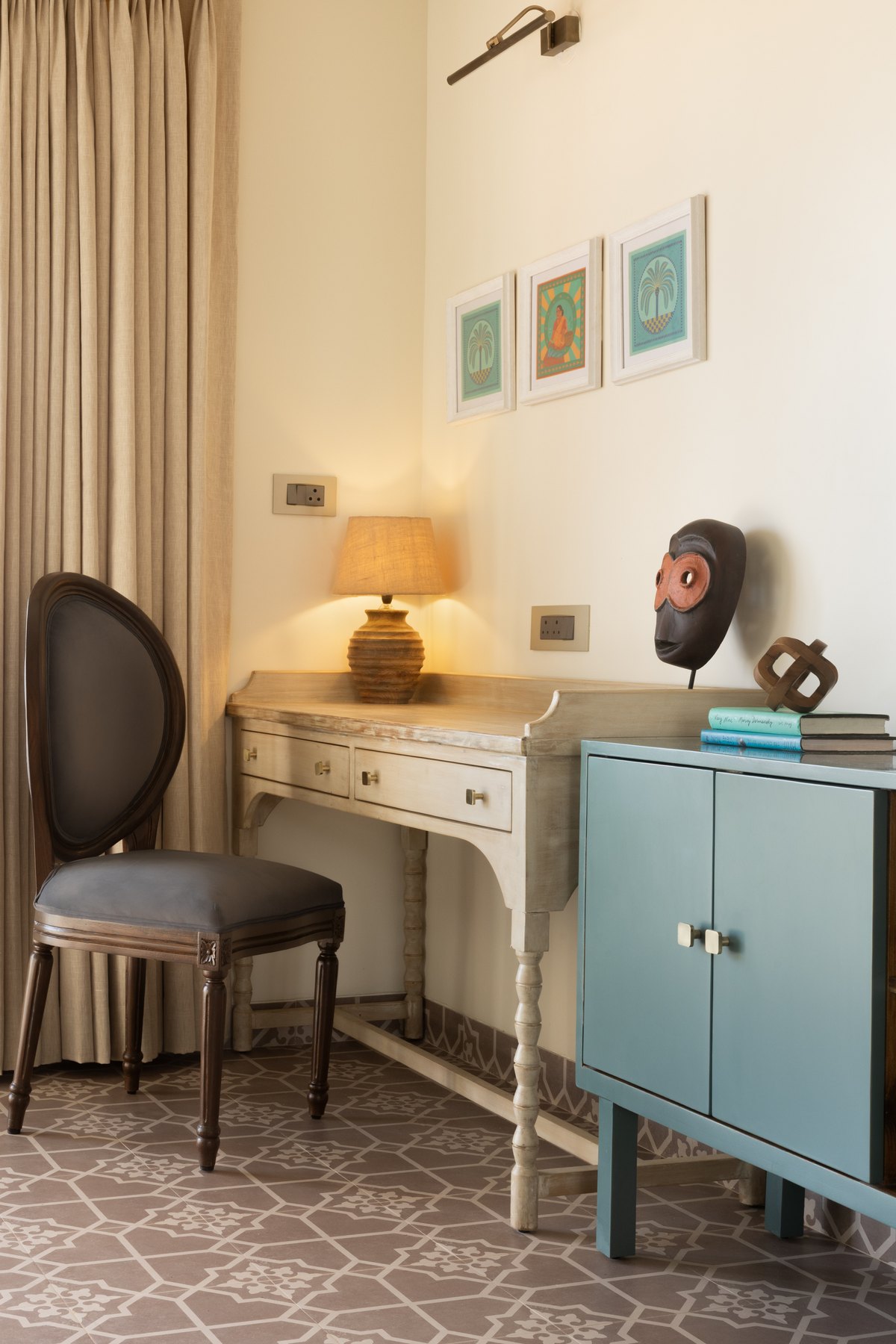 Carved writing desk and pale blue cabinet below framed prints