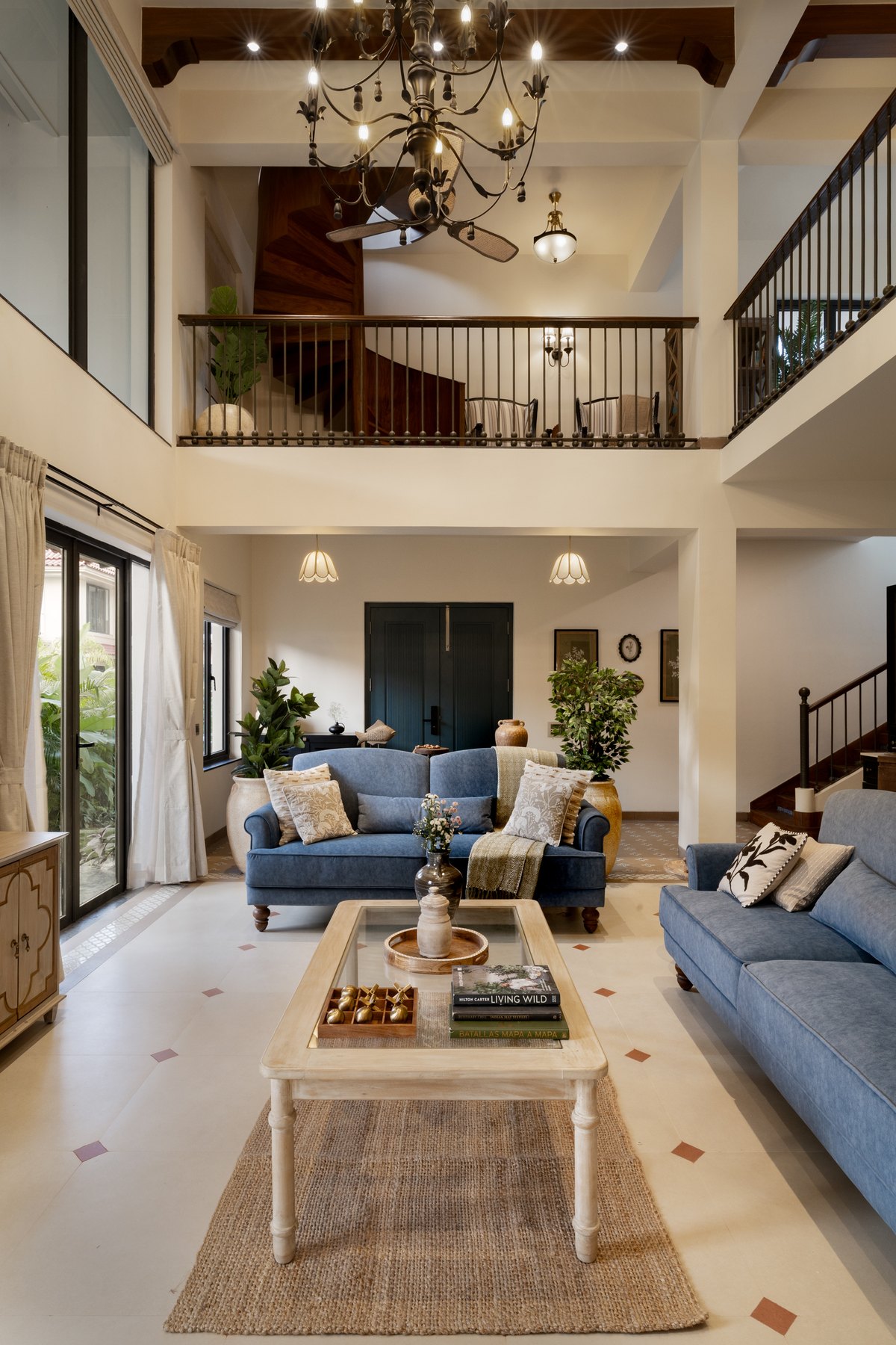 Double-height living room under a wrought-iron chandelier, with the mezzanine landing above