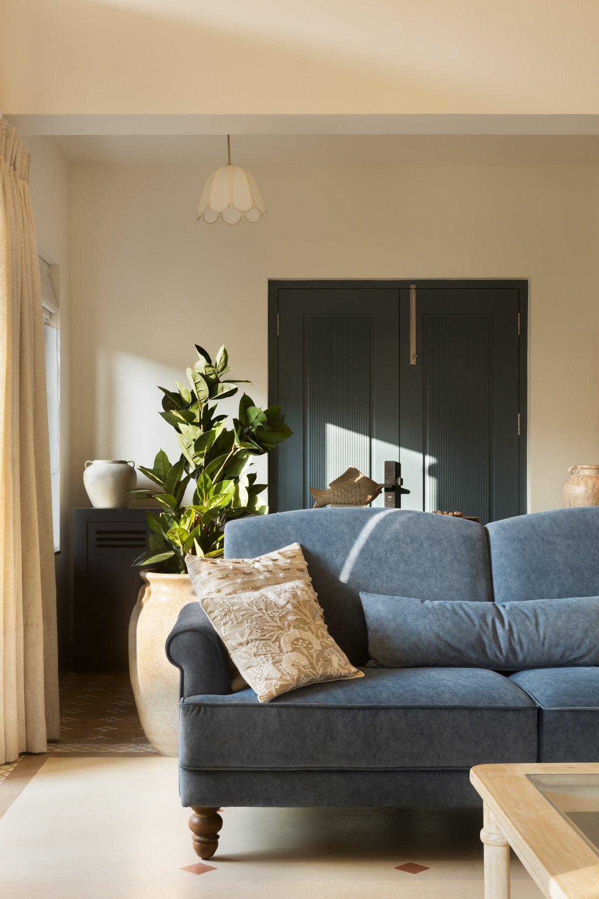 Blue sofa beside the deep green entrance doors and a potted fig in a stone urn