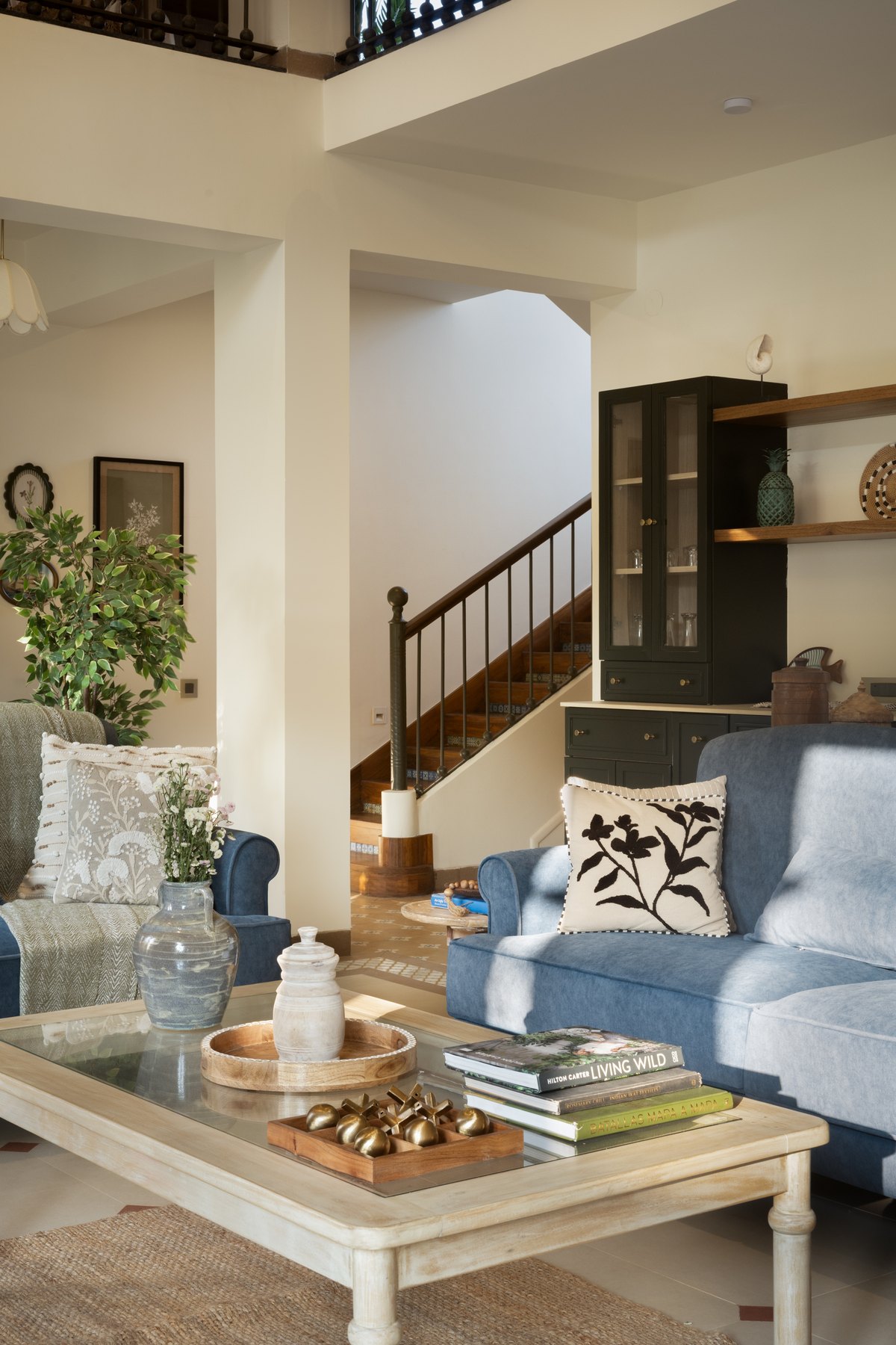 Blue sofa and glass-topped table in front of the open stair and dark shelving