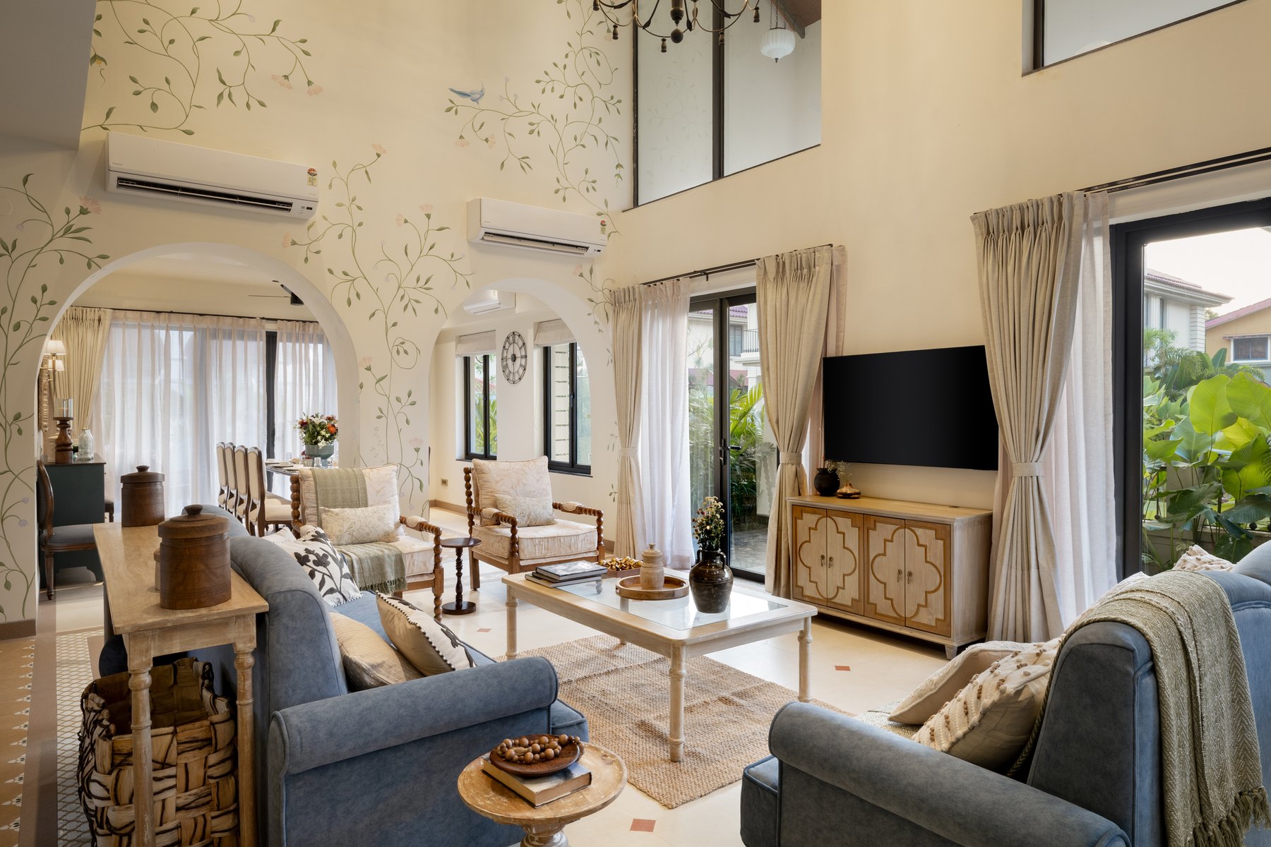 The living room along its length, vines painted across the far wall above the seating