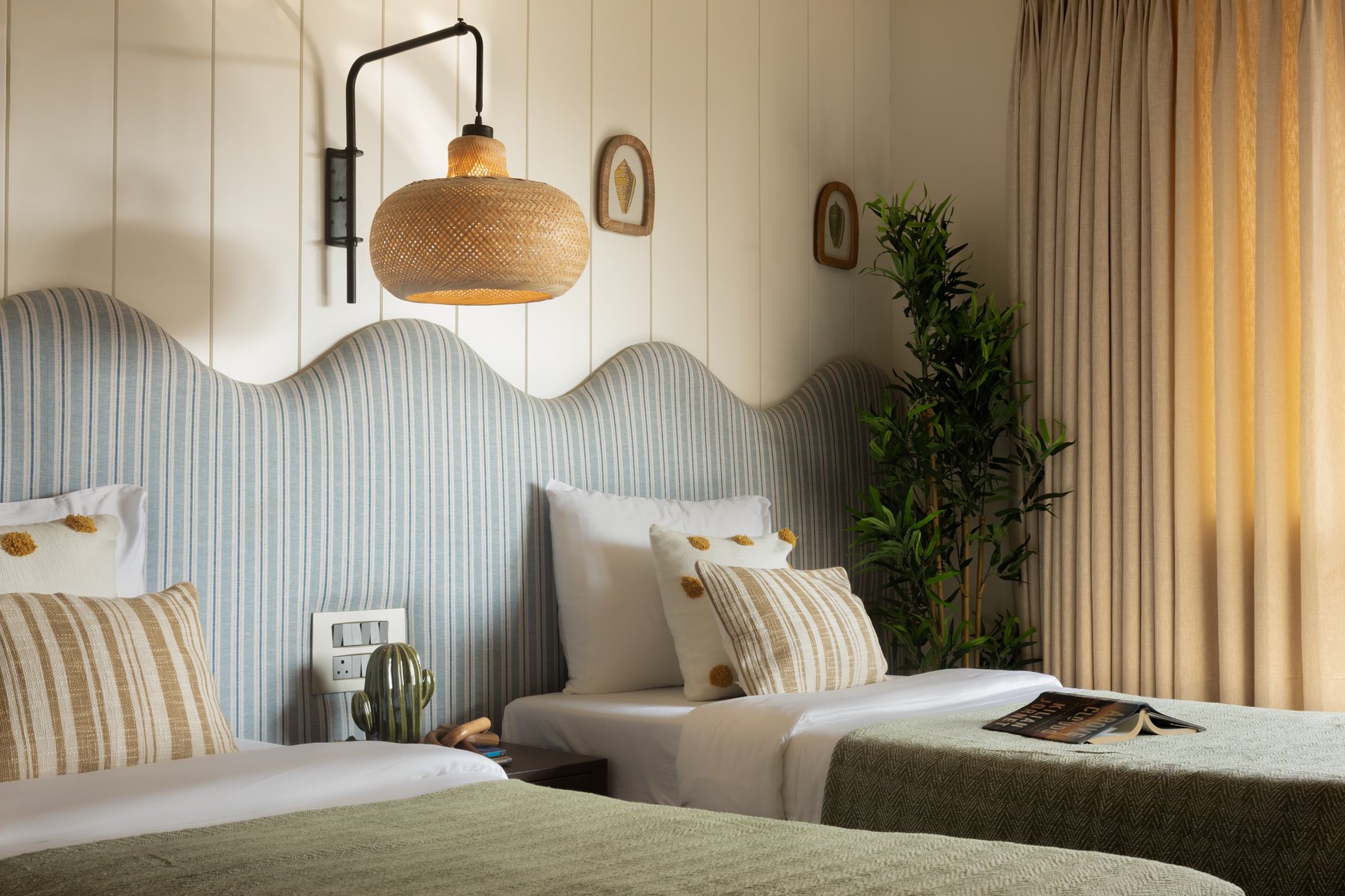Twin beds in green below a woven pendant and the scalloped headboard