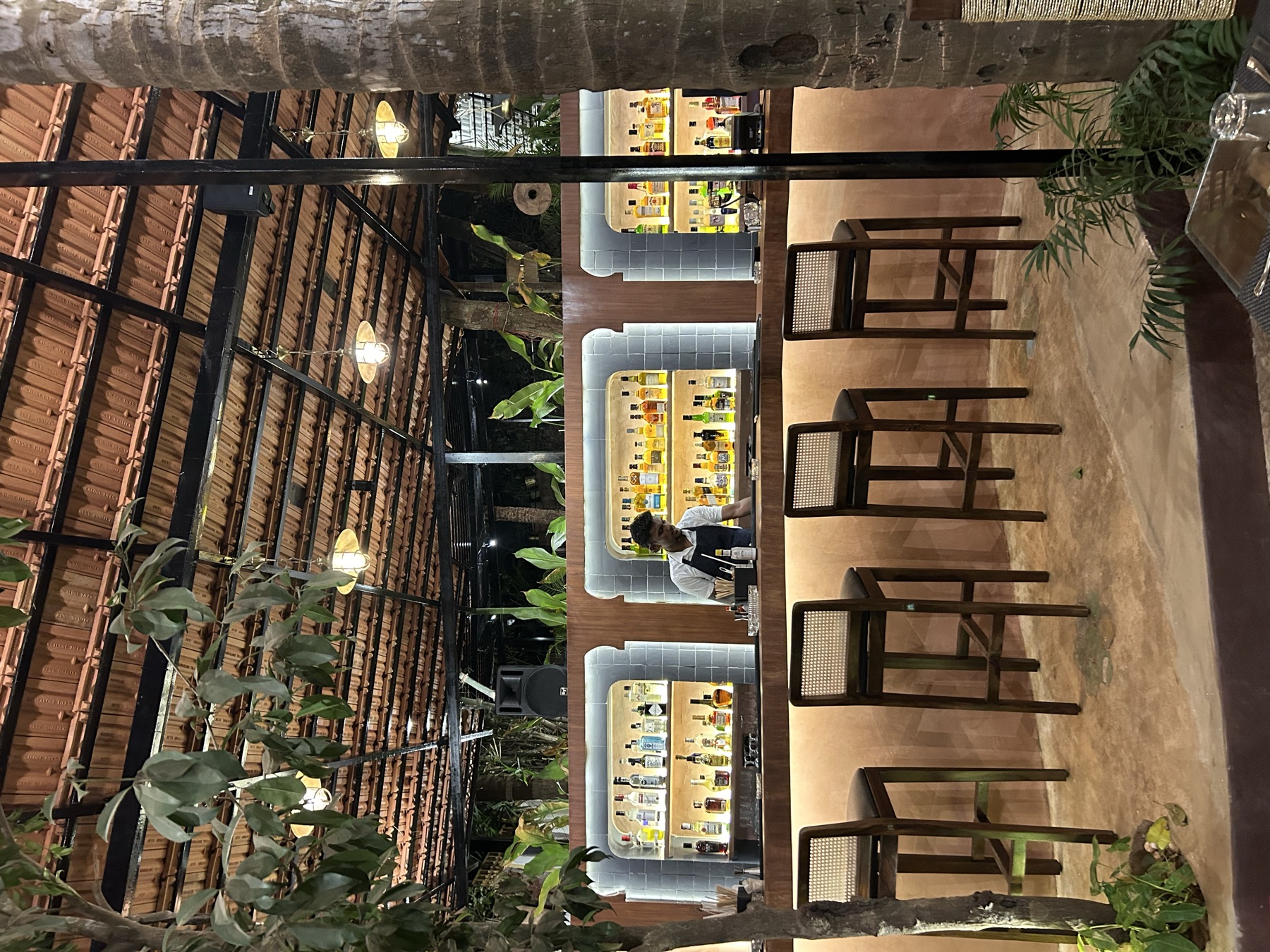 Cane stools along the lit bar counter at night, under the clay-tiled roof