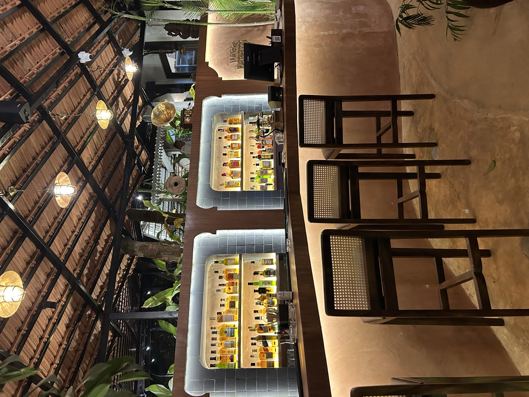 The full length of the backbar, its arched niches lit behind cane stools