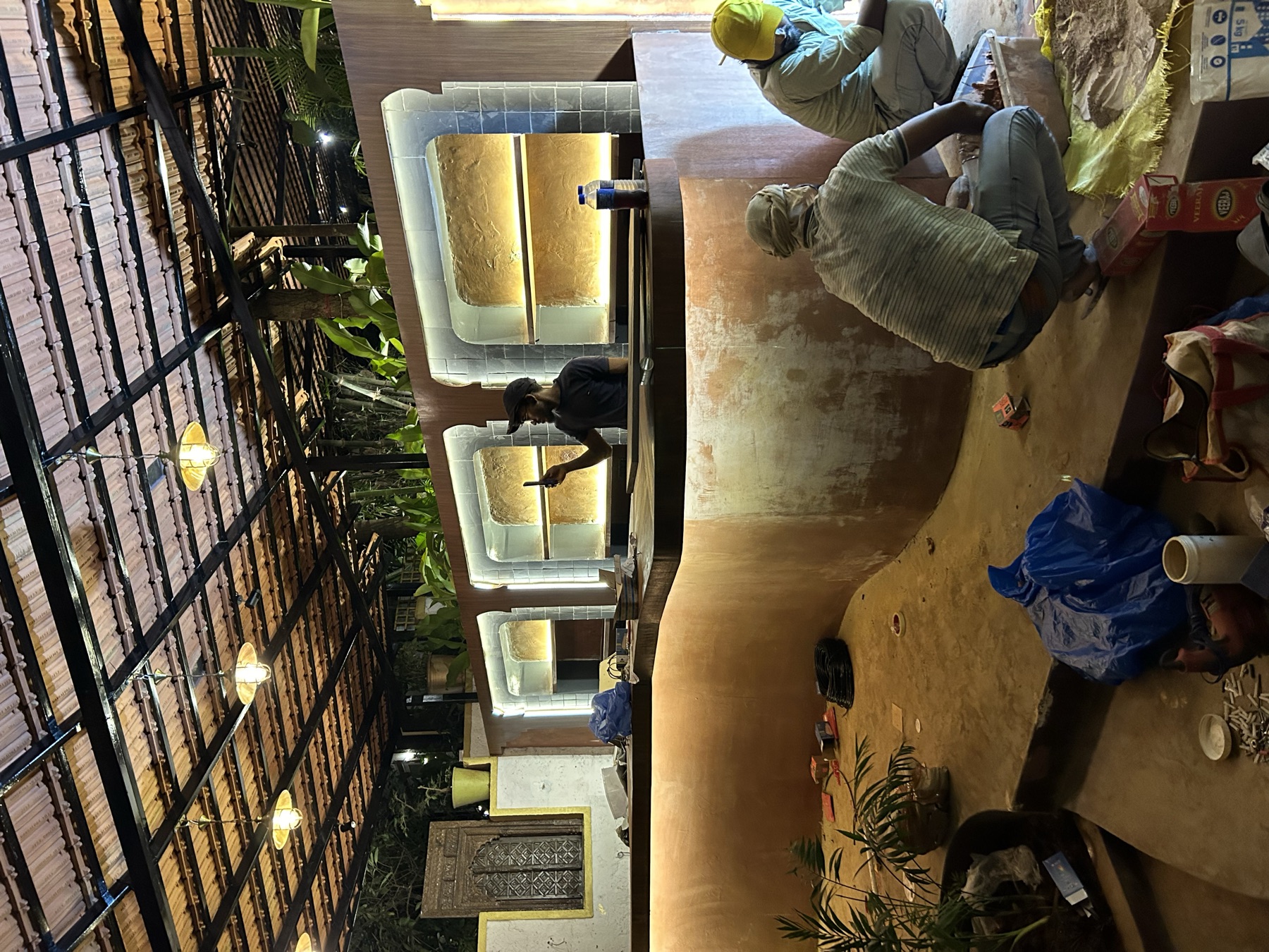 Artisans hand-finishing the plaster counter as the backbar shelves are lit for the first time